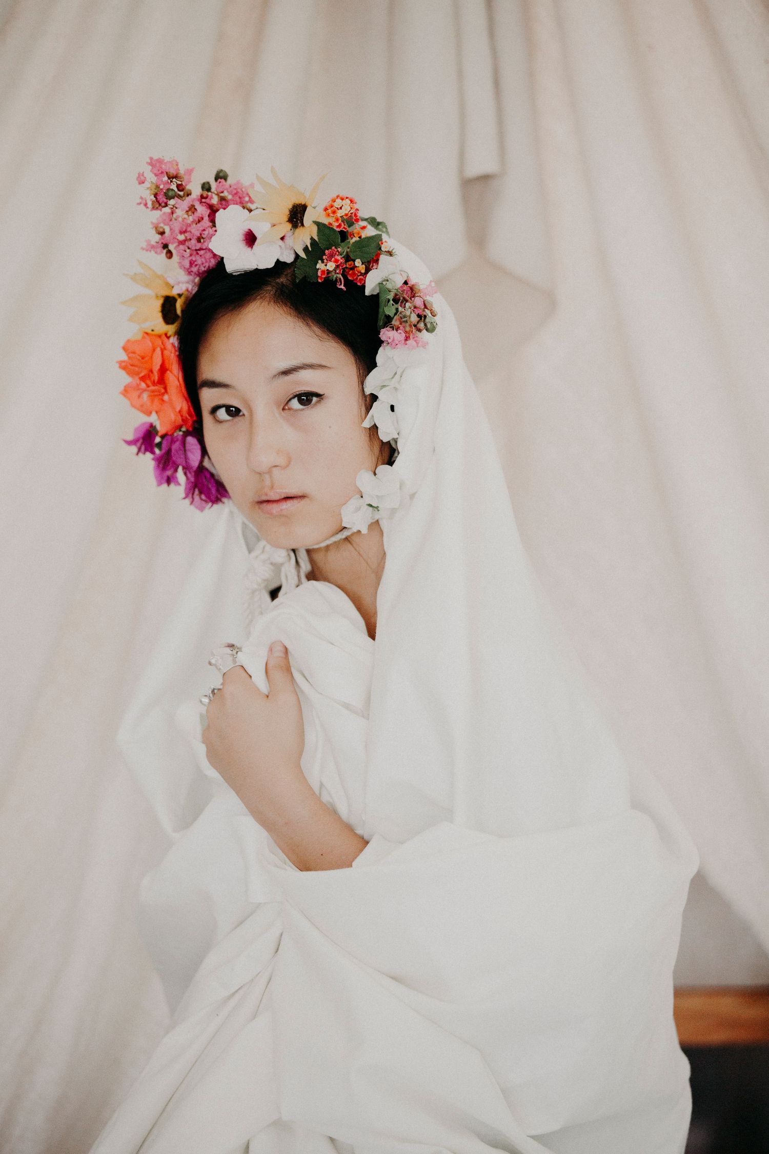 Editorial portrait in Los Angeles, CA featuring a woman in white with a colorful floral headpiece against a soft backdrop