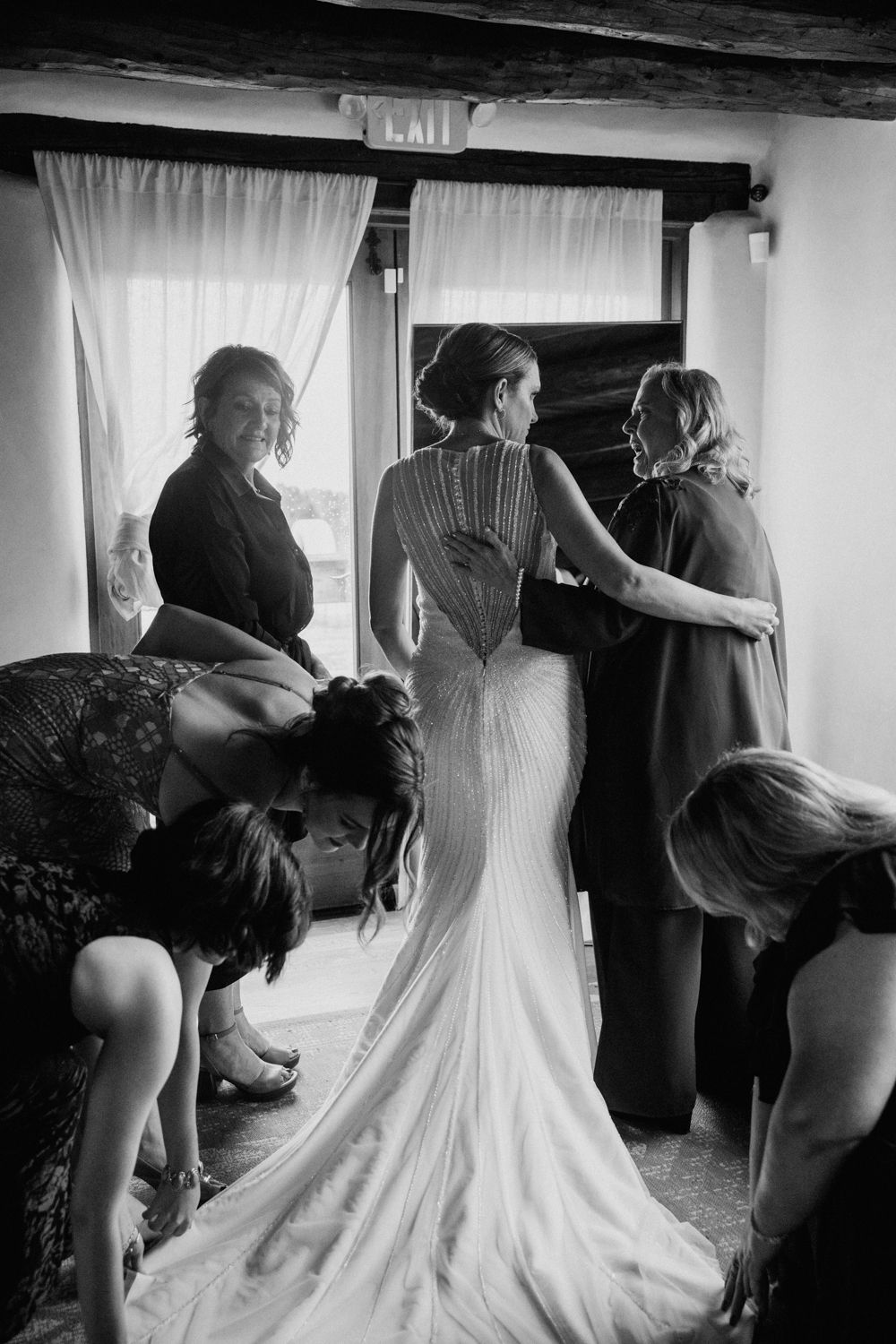 A series of black and white photos showing the preparation and buttoning up of an elegant wedding dress.