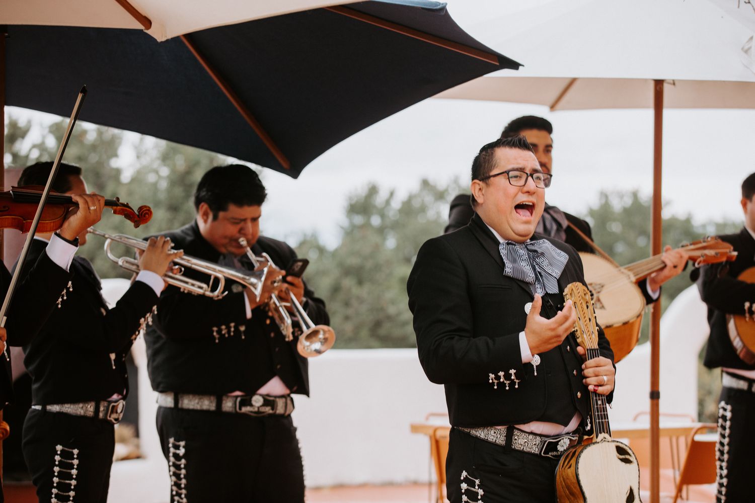 Mariachi band performs under umbrellas at an outdoor celebration.