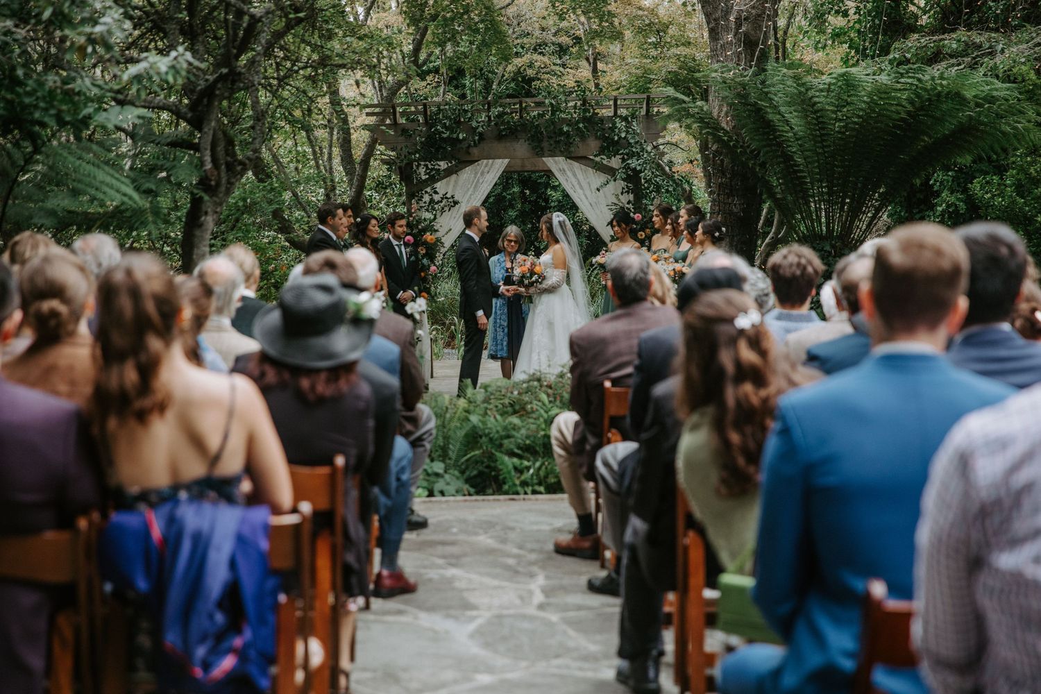 Outdoor wedding ceremony in a garden setting with rows of wooden chairs.