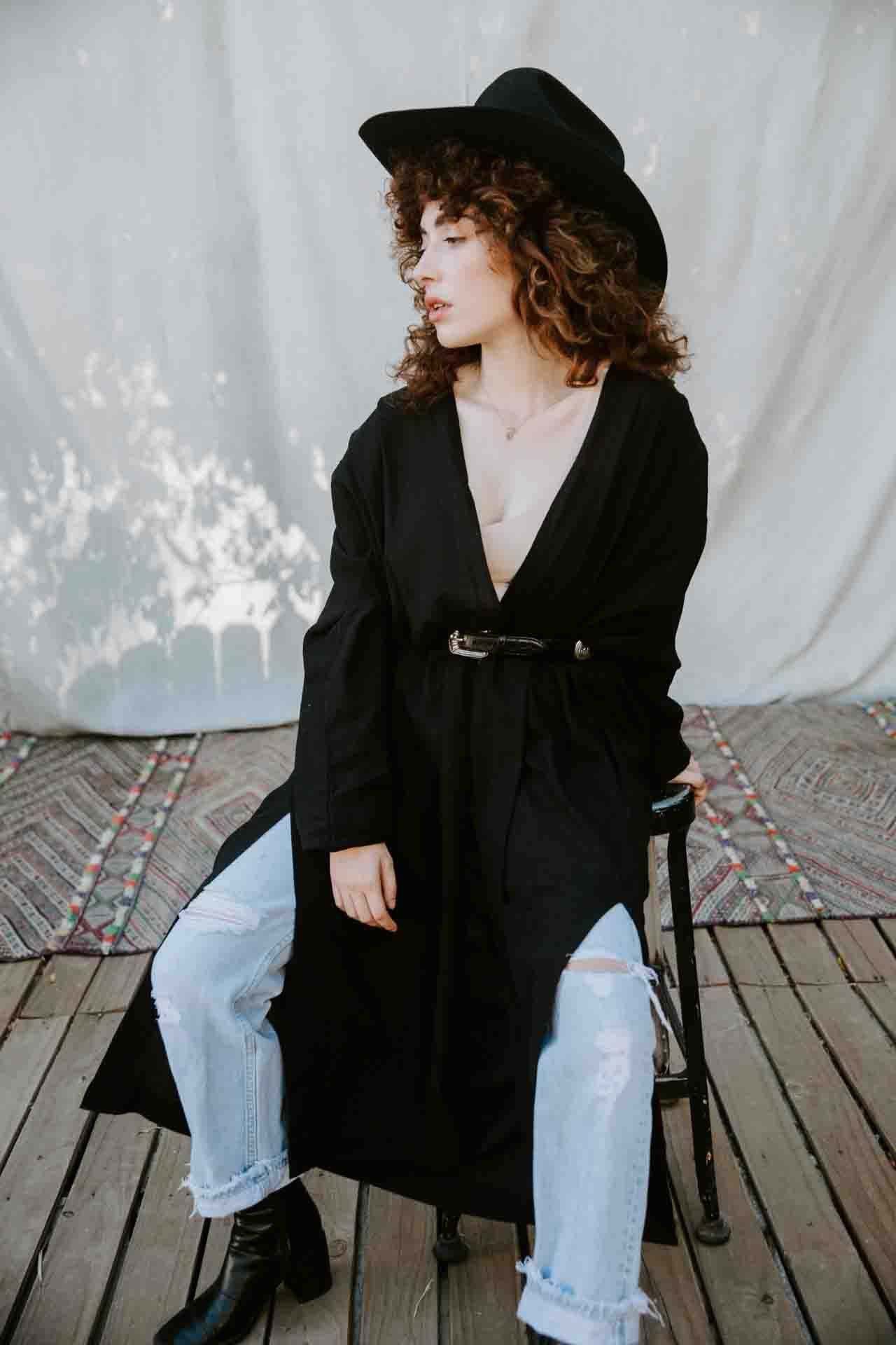 Person in black blazer and light denim jeans poses against white backdrop in artistic photo series.