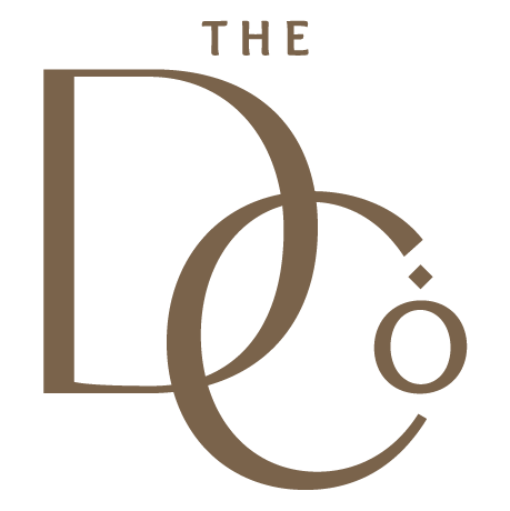 The DCo logo featuring elegant serif typography in warm brown tones with a decorative dot accent.