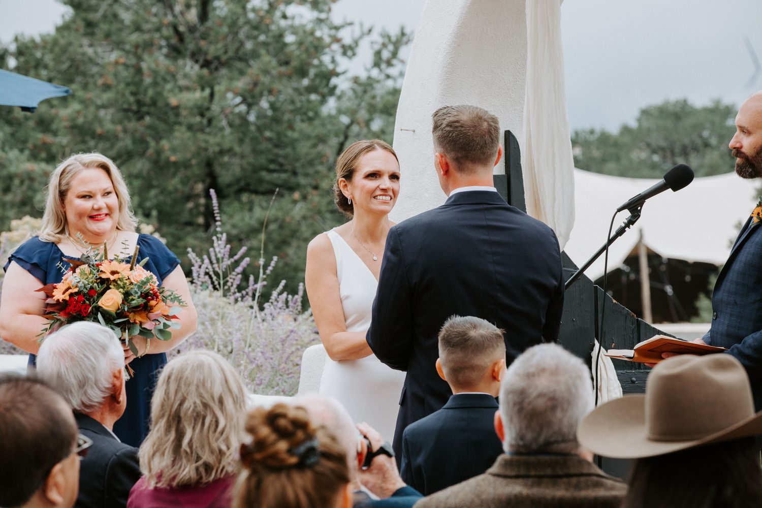 Wedding ceremony guests seated outdoors with natural scenery in background.