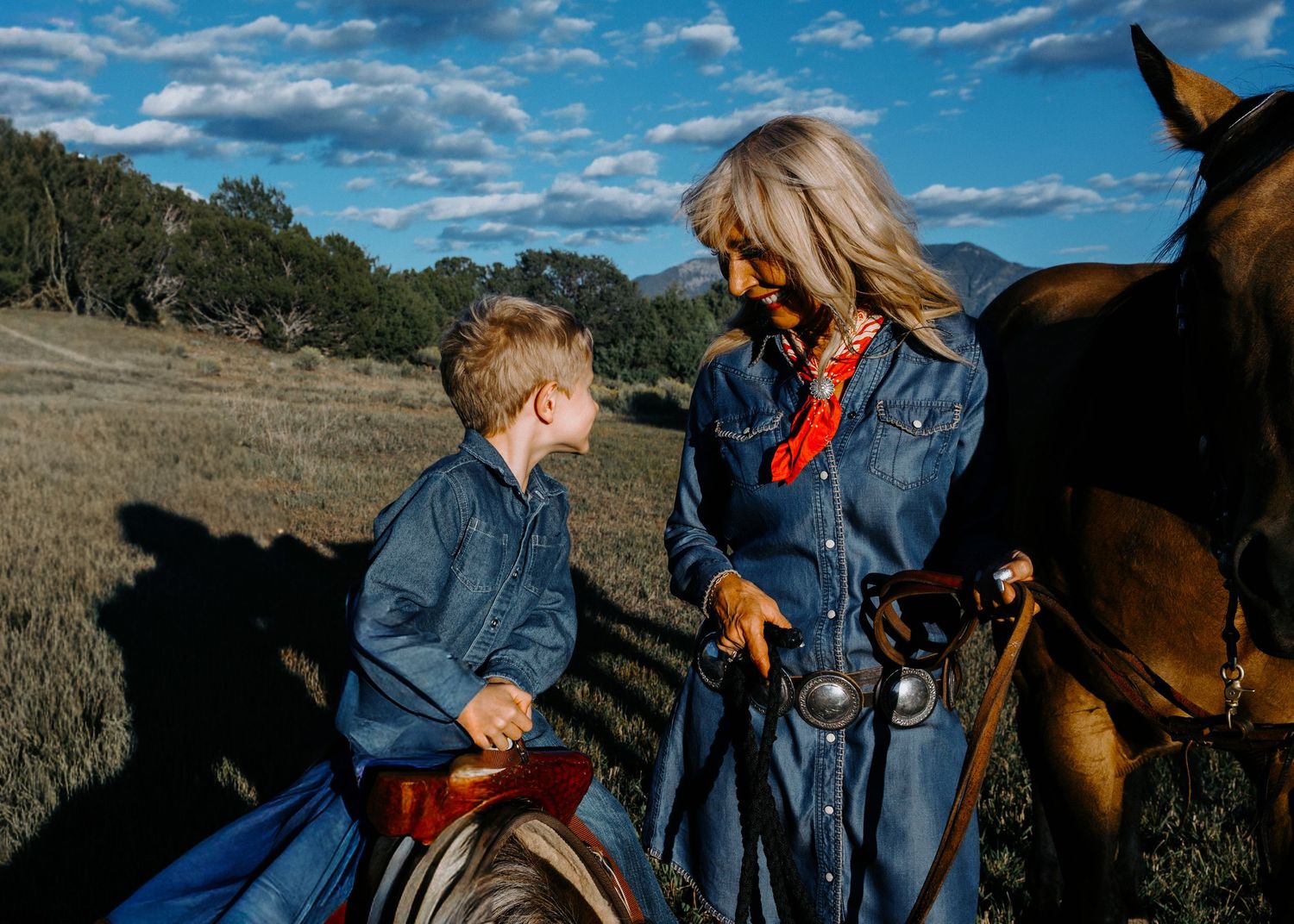 Family session in Taos NM with grandmother and grandson near a horse in a sunlit mountain landscape