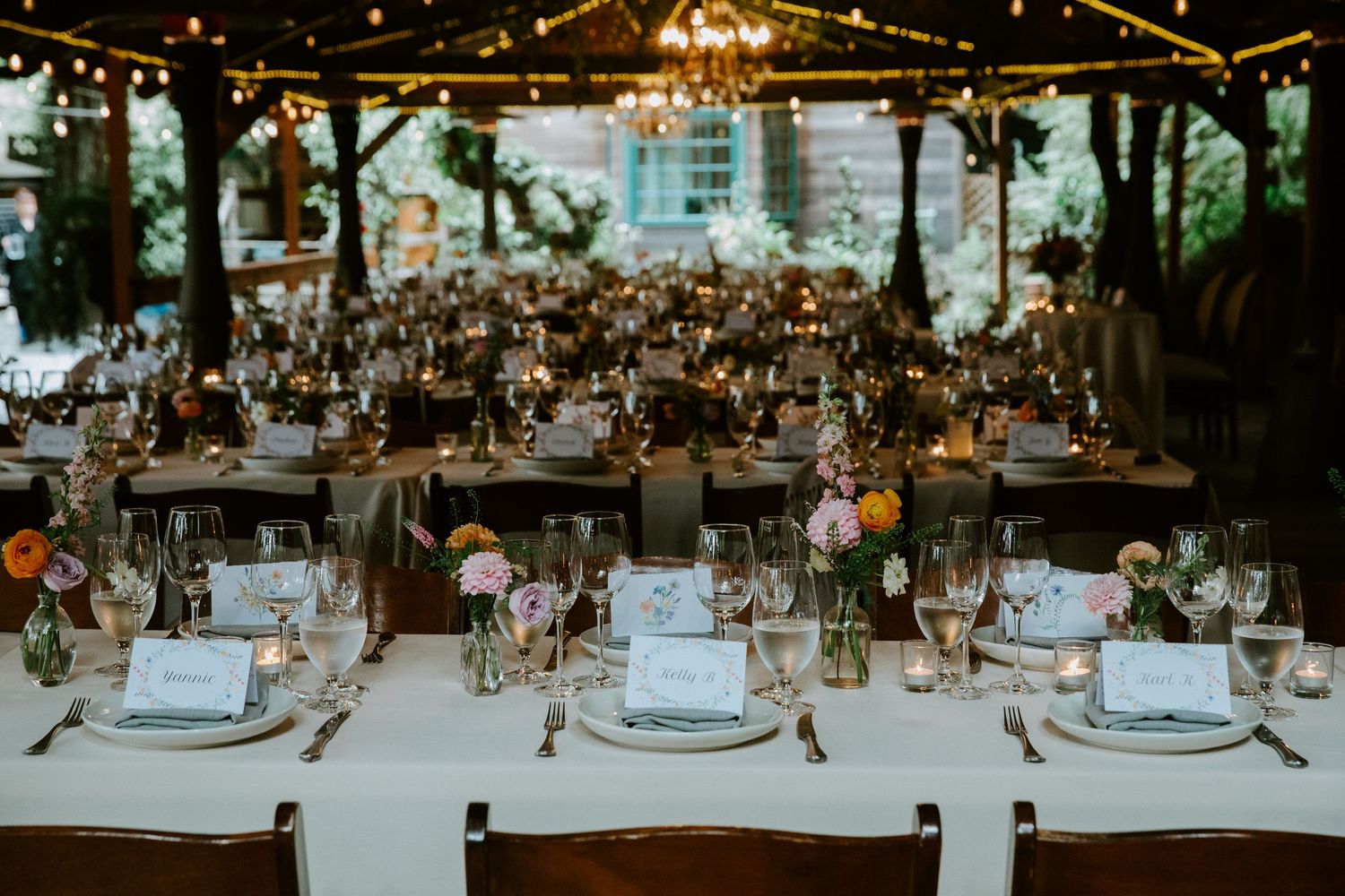 Elegant outdoor wedding reception setup with string lights and table settings in a garden venue.