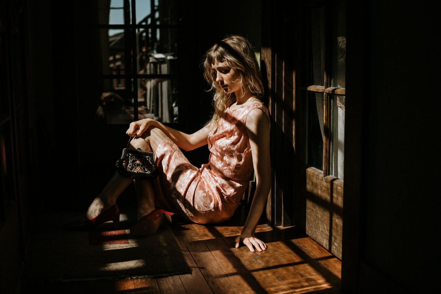 Artistic portrait in vintage setting with dramatic shadows falling through wooden slats onto pink dress.