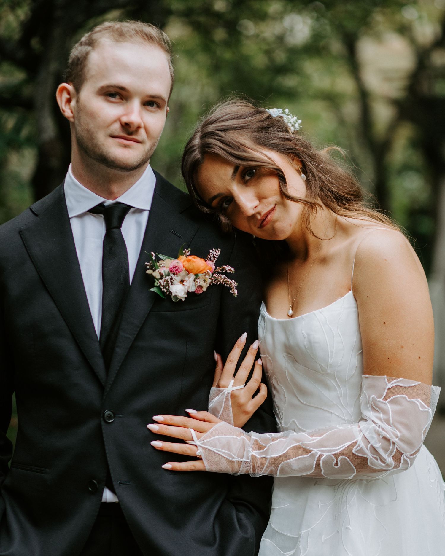 A couple shares an intimate moment in formal wedding attire surrounded by greenery.