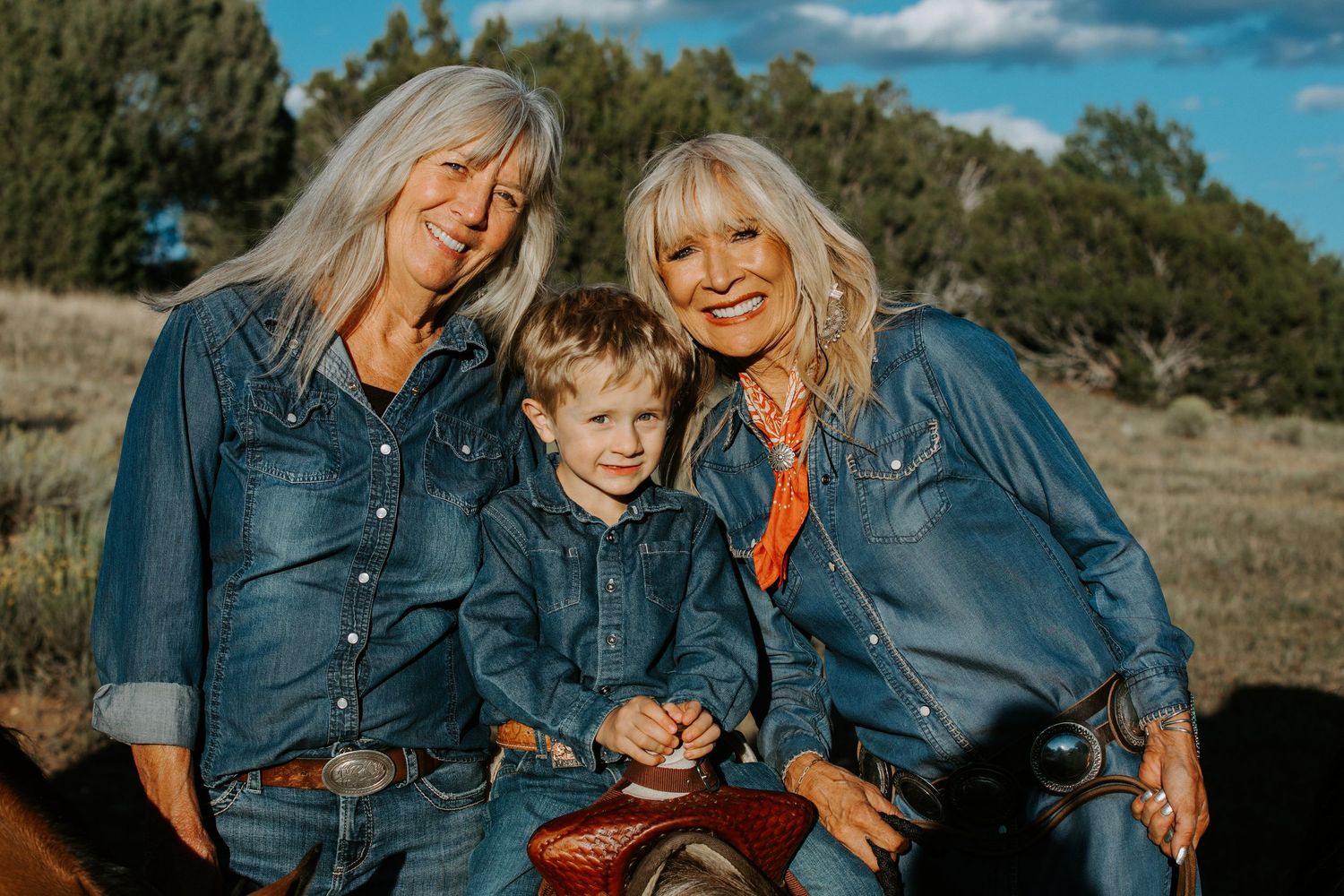 A family in denim clothing poses together on a grassy hillside during a sunny autumn day.