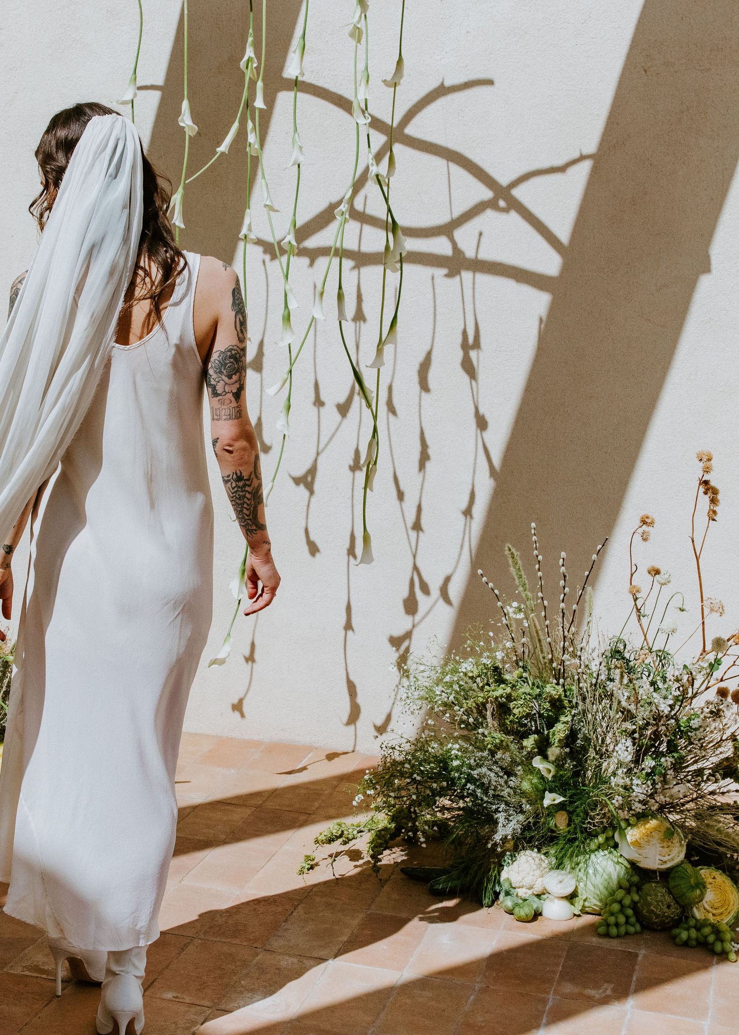 White floral arrangements and greenery decorate a light-filled venue with natural shadows on the wall.