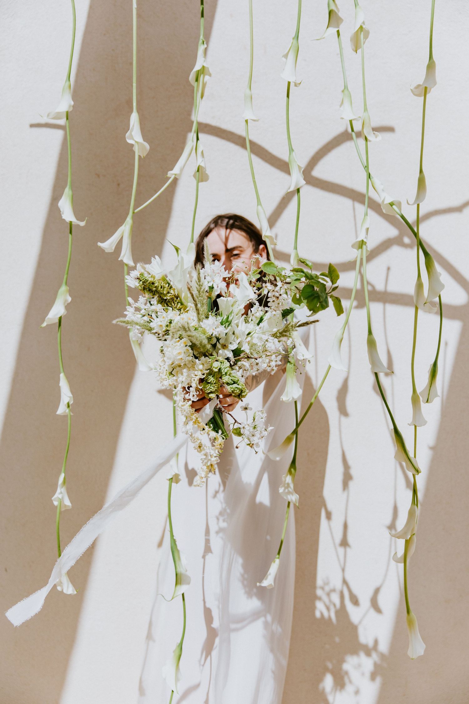 White floral arrangements with cascading flowers and greenery hang against a light beige wall creating an ethereal backdrop.