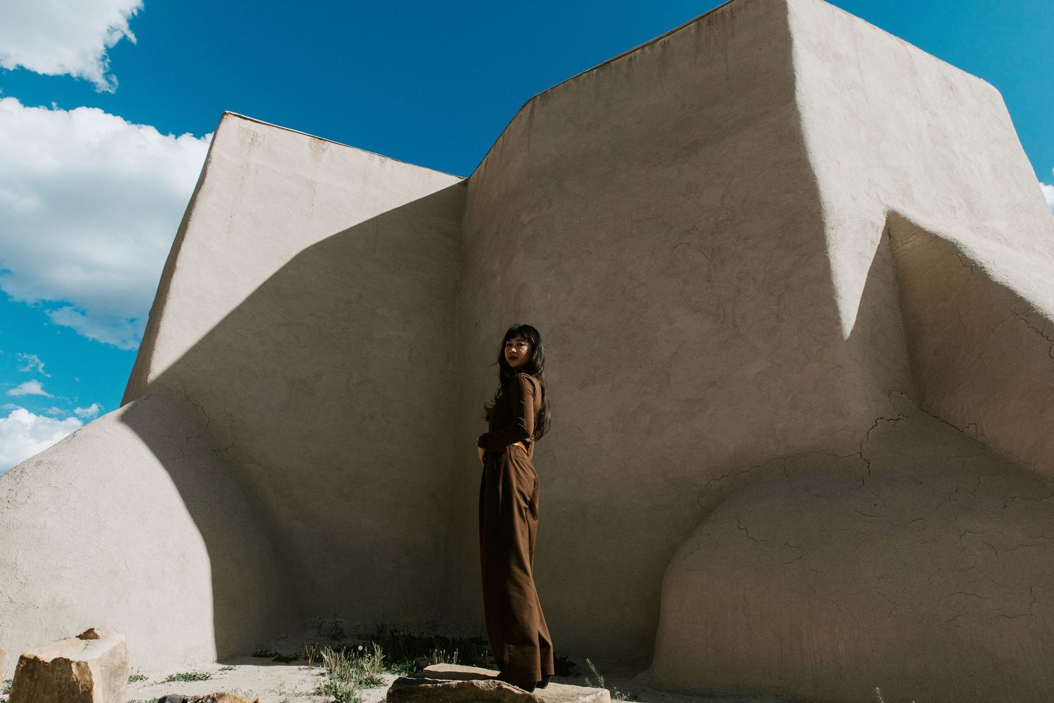 Woman in brown outfit standing against white adobe walls under blue sky.