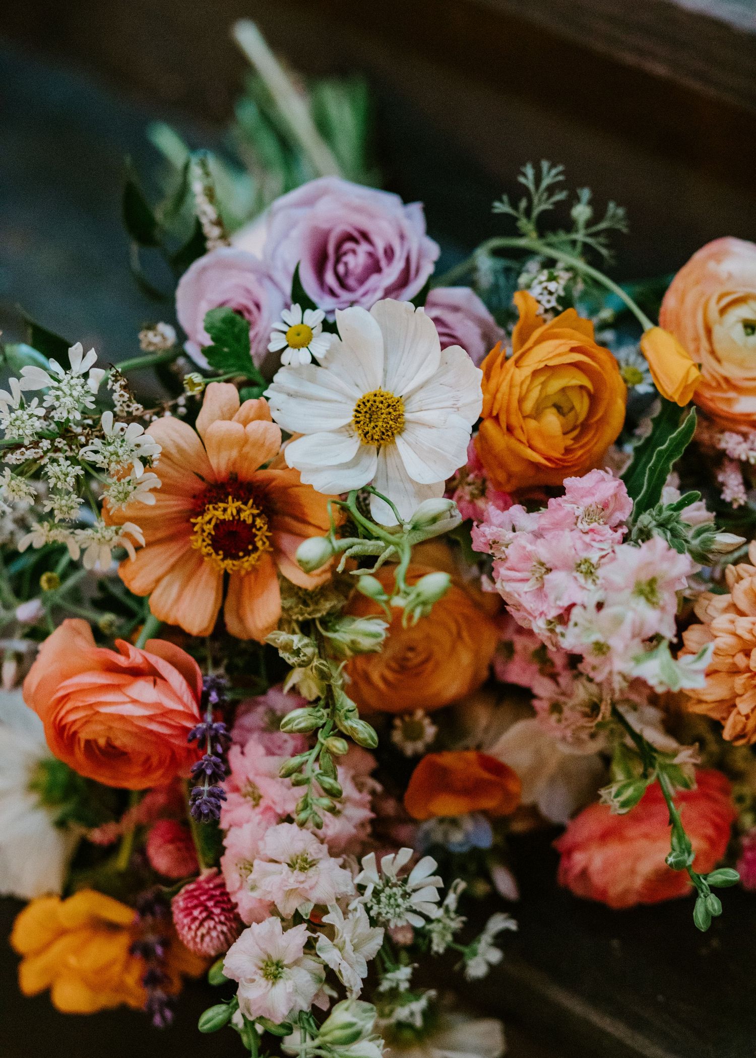 Colorful wedding bouquet with orange, pink and white flowers arranged with greenery and delicate details.