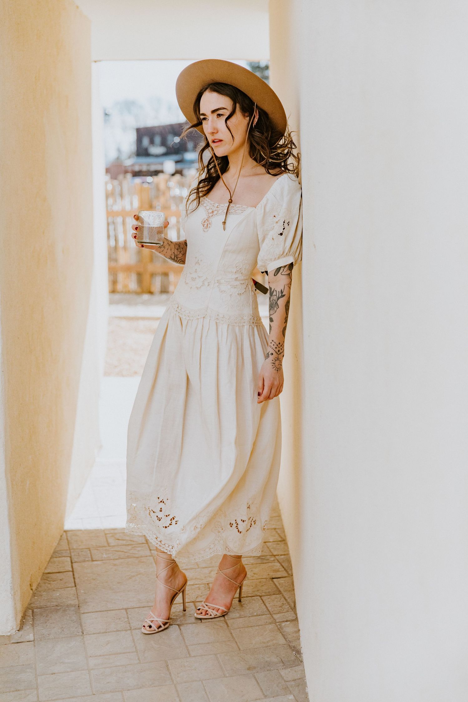 A white flowy summer dress is styled with neutral sandals in a bright interior setting with pillars.