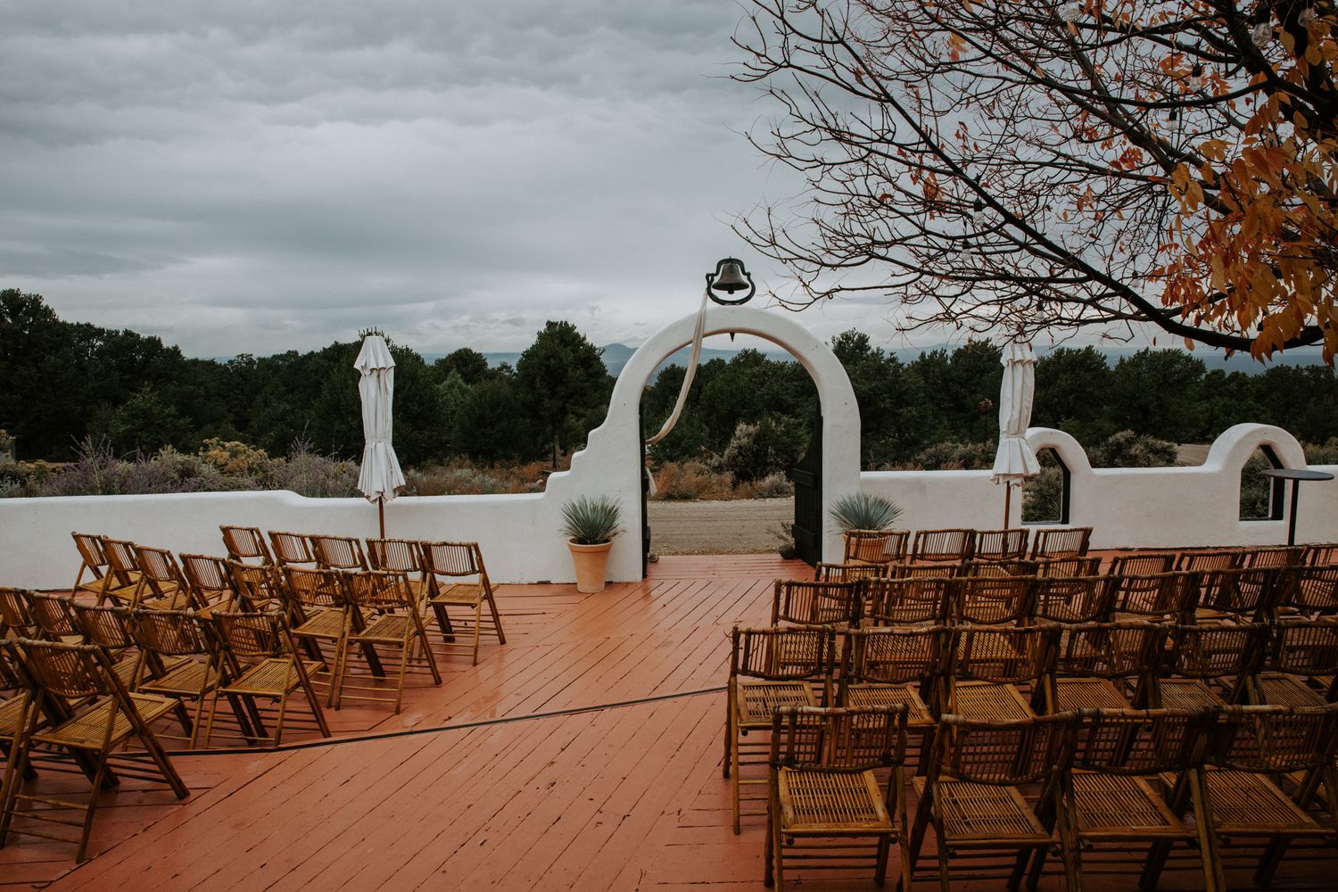 Rows of wooden chairs arranged outdoors for a wedding ceremony with mountain views and cloudy skies.