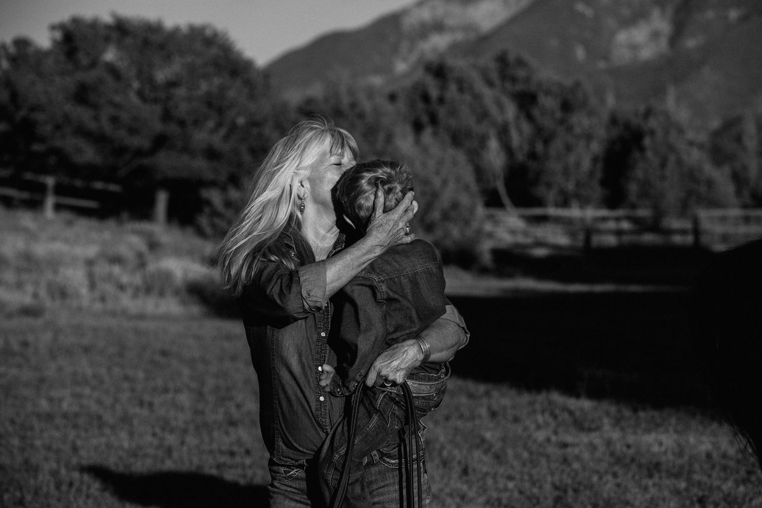 A tender moment captured in black and white outdoors with mountains and trees in the background.