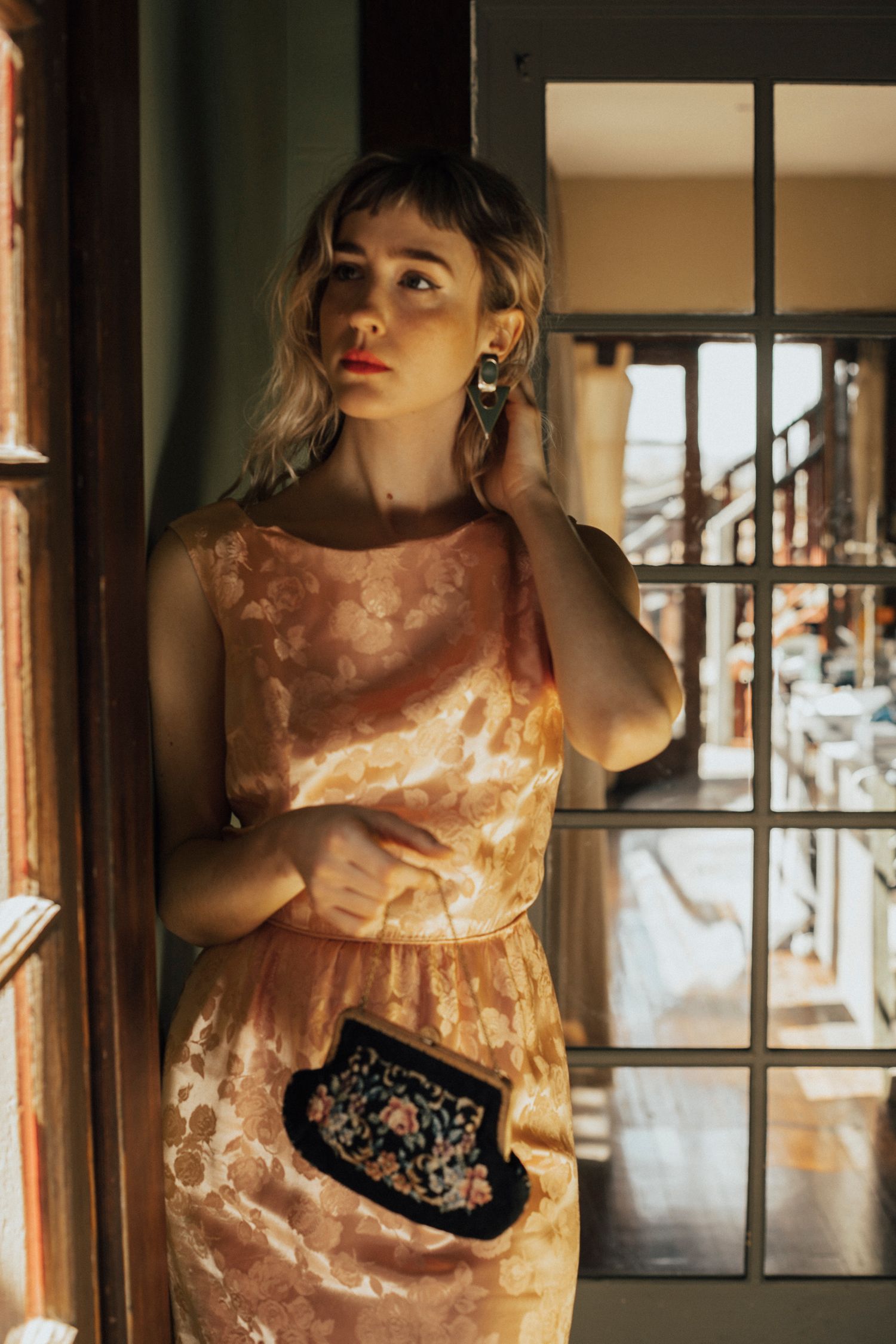 Fashion portrait series showing a warm-toned dress against wooden interior panels in moody lighting.