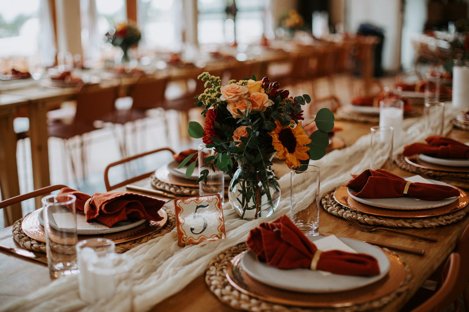 Long reception table with burgundy place settings and floral centerpieces in warm lighting.