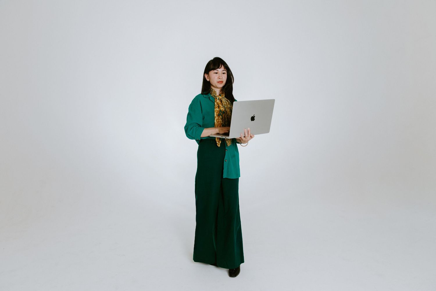 Woman in green outfit holding a silver laptop, standing against a white background.