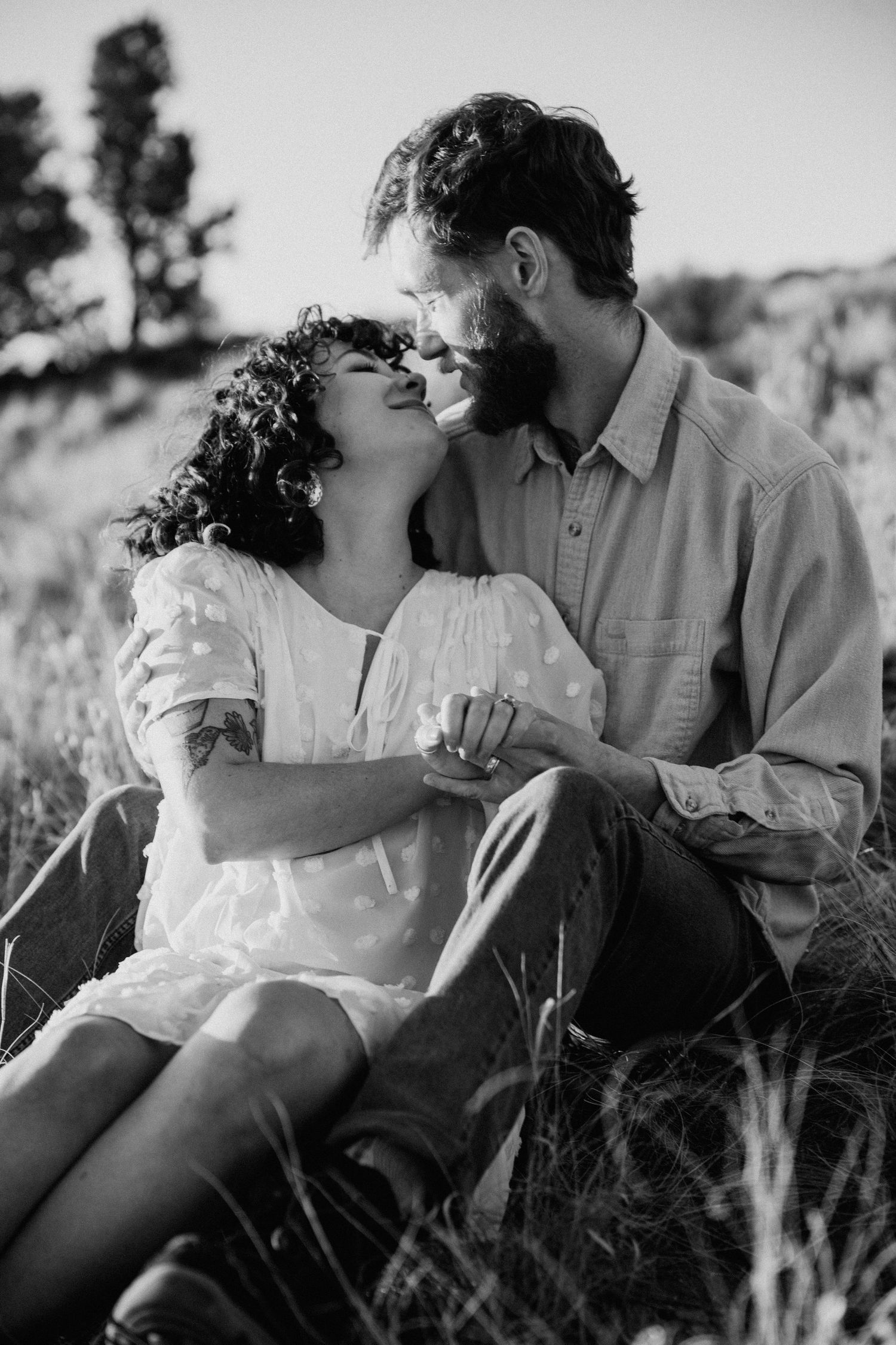 Black and white engagement session in Taos NM with couple relaxing together in a sunlit grassy field