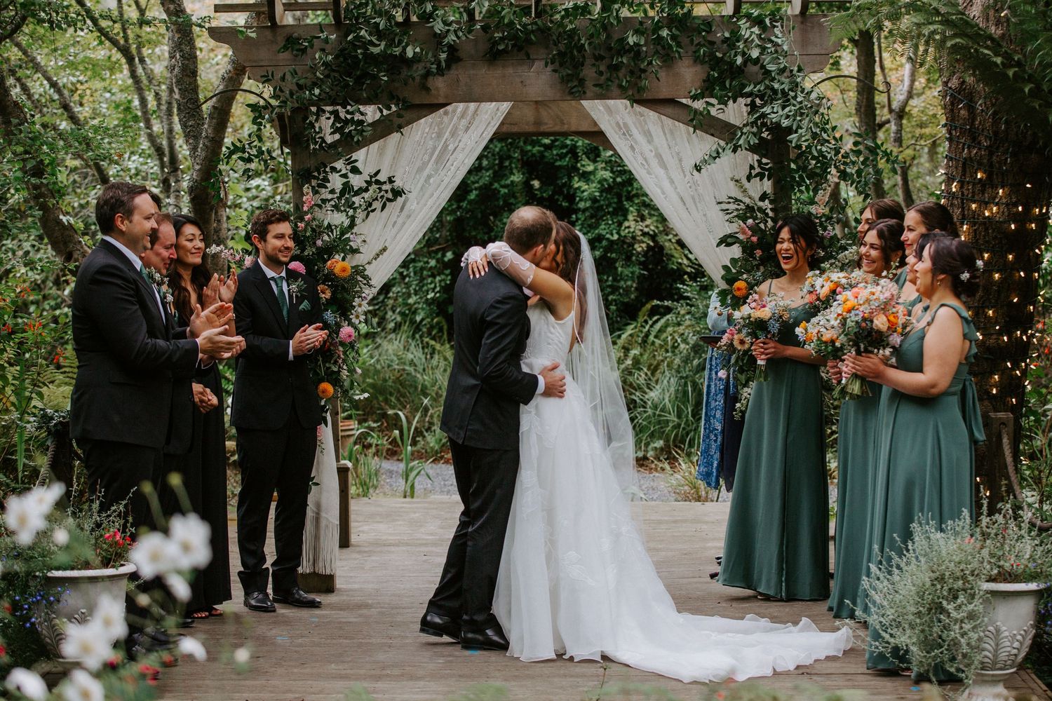 Outdoor wedding ceremony under white fabric arch surrounded by lush greenery and trees.
