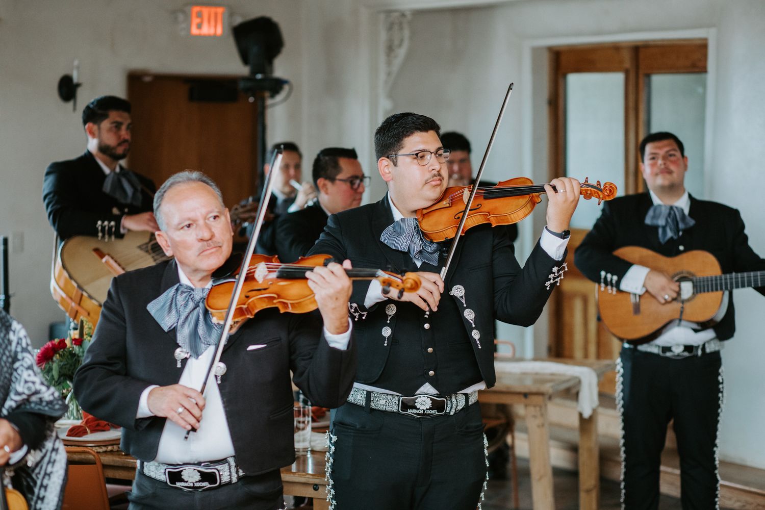 Orchestra musicians perform together while playing violins in a bright indoor venue.
