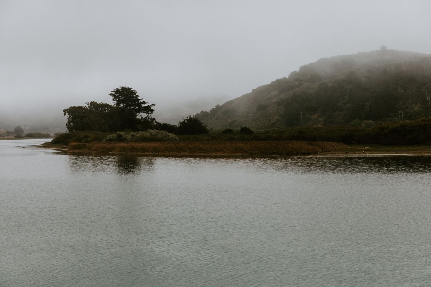 A serene panoramic view of a foggy coastal landscape with rocky shores and small islands in the distance.