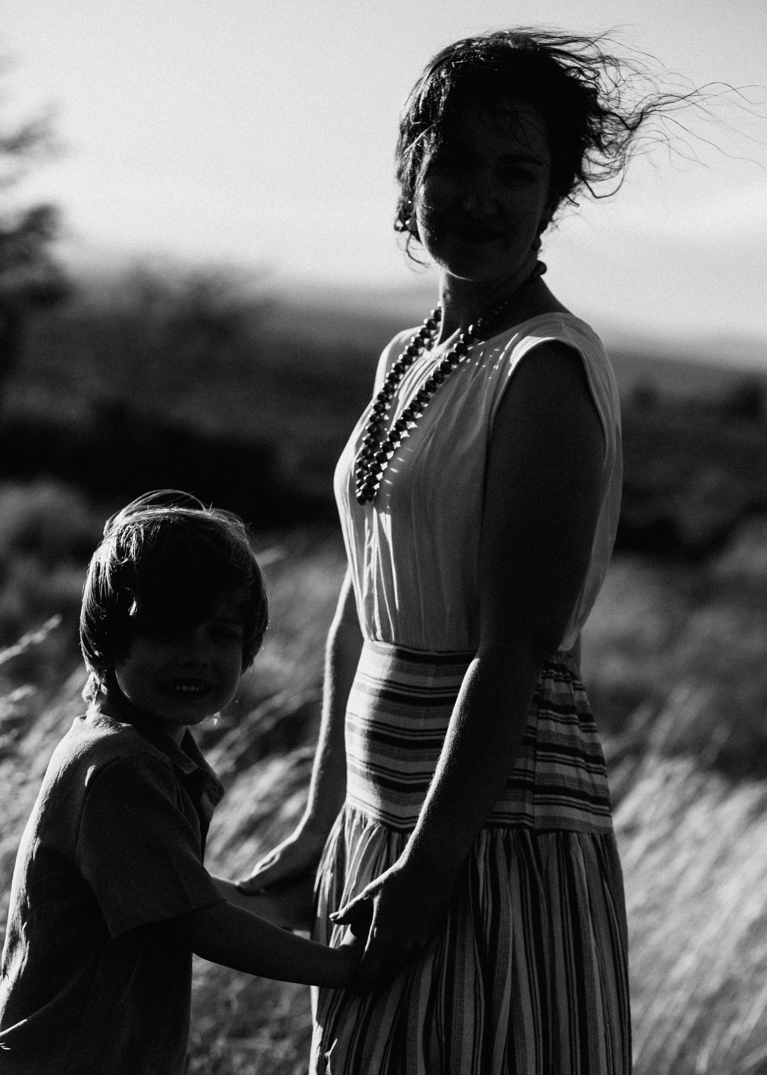 Black and white portrait series shows tender interactions between family members in windswept field.