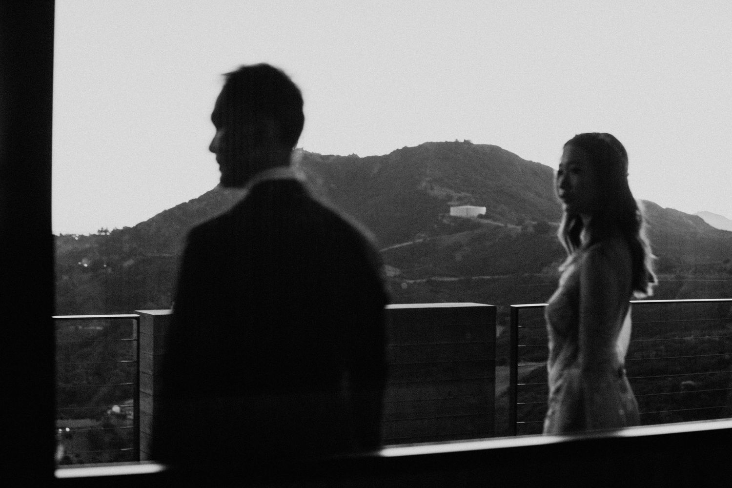 Silhouetted couple stands on balcony overlooking mountain landscape at sunset in black and white.  Shot in California, by Siouxzen Kang