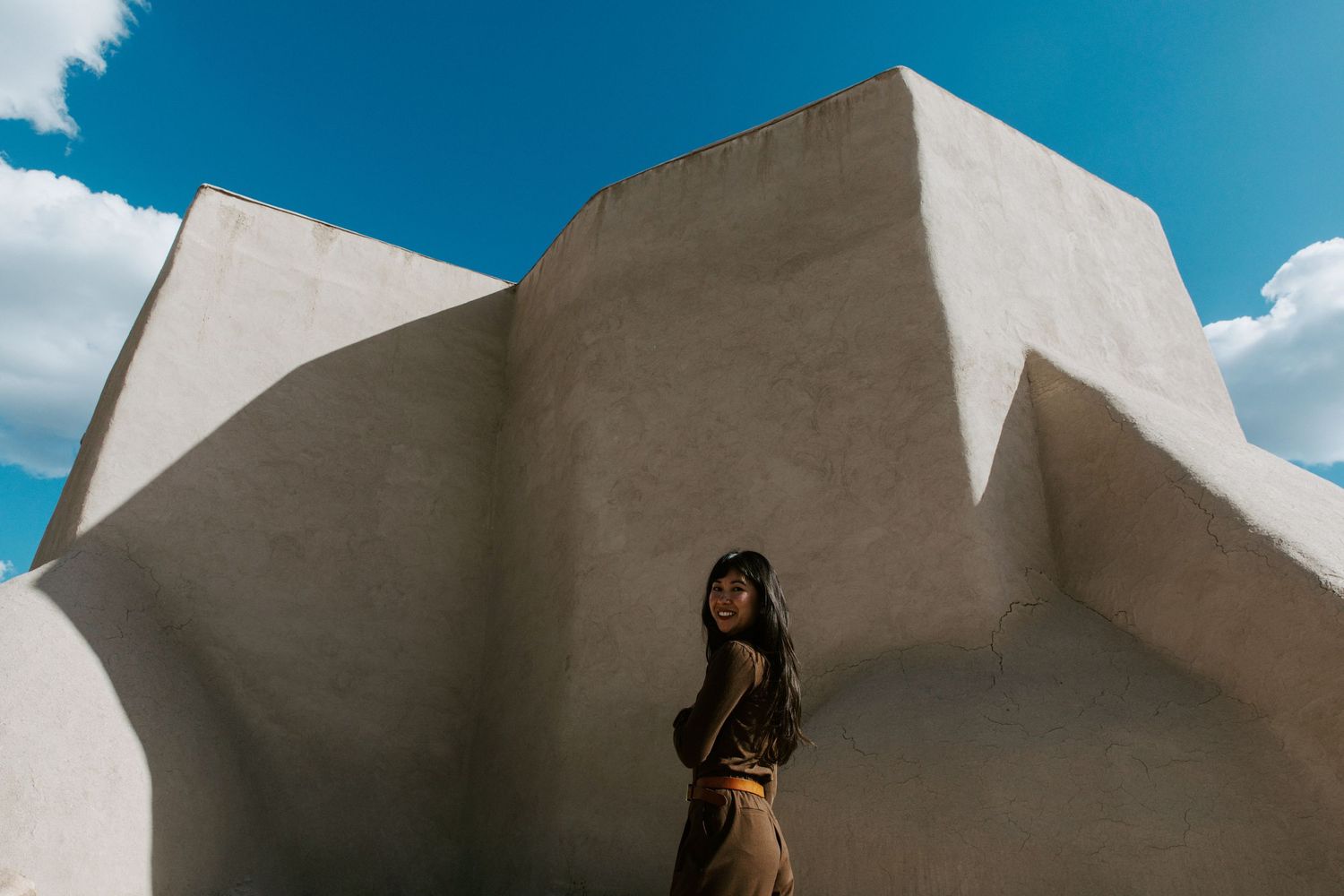 Woman standing against white adobe architecture under blue sky.