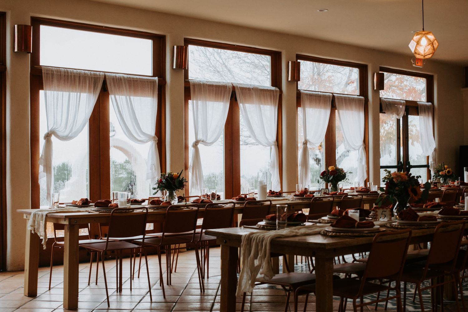 A bright and spacious restaurant interior with large windows, wooden furniture and pendant lighting creates an elegant dining atmosphere.