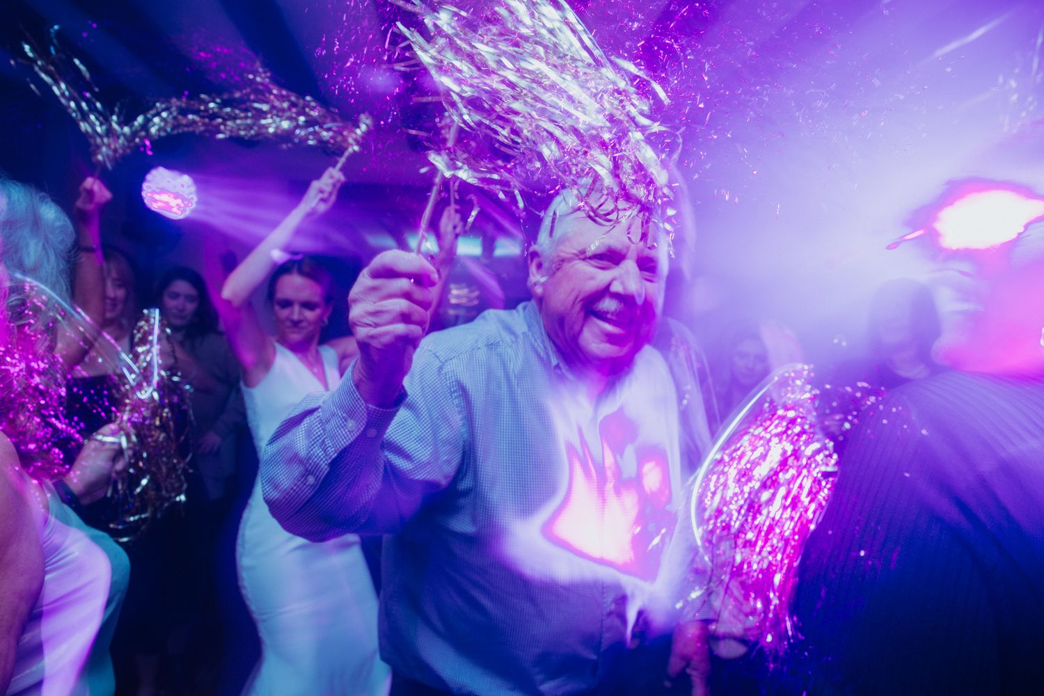 People dancing and celebrating at a nightclub with vibrant purple lighting effects creating an energetic atmosphere.