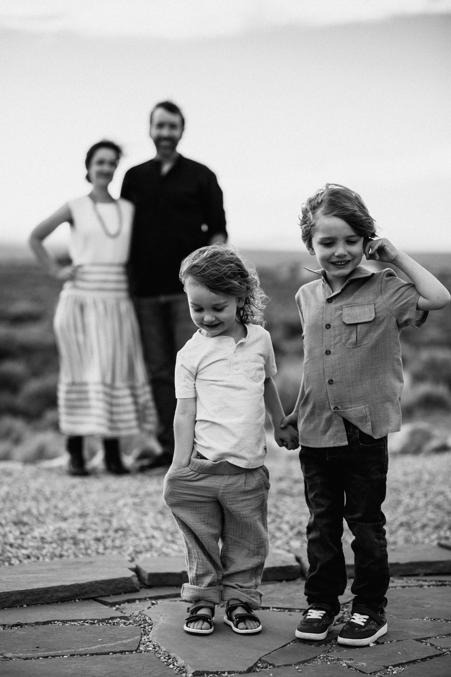 Black and white family portrait showing two children standing on stone path with adults in background.