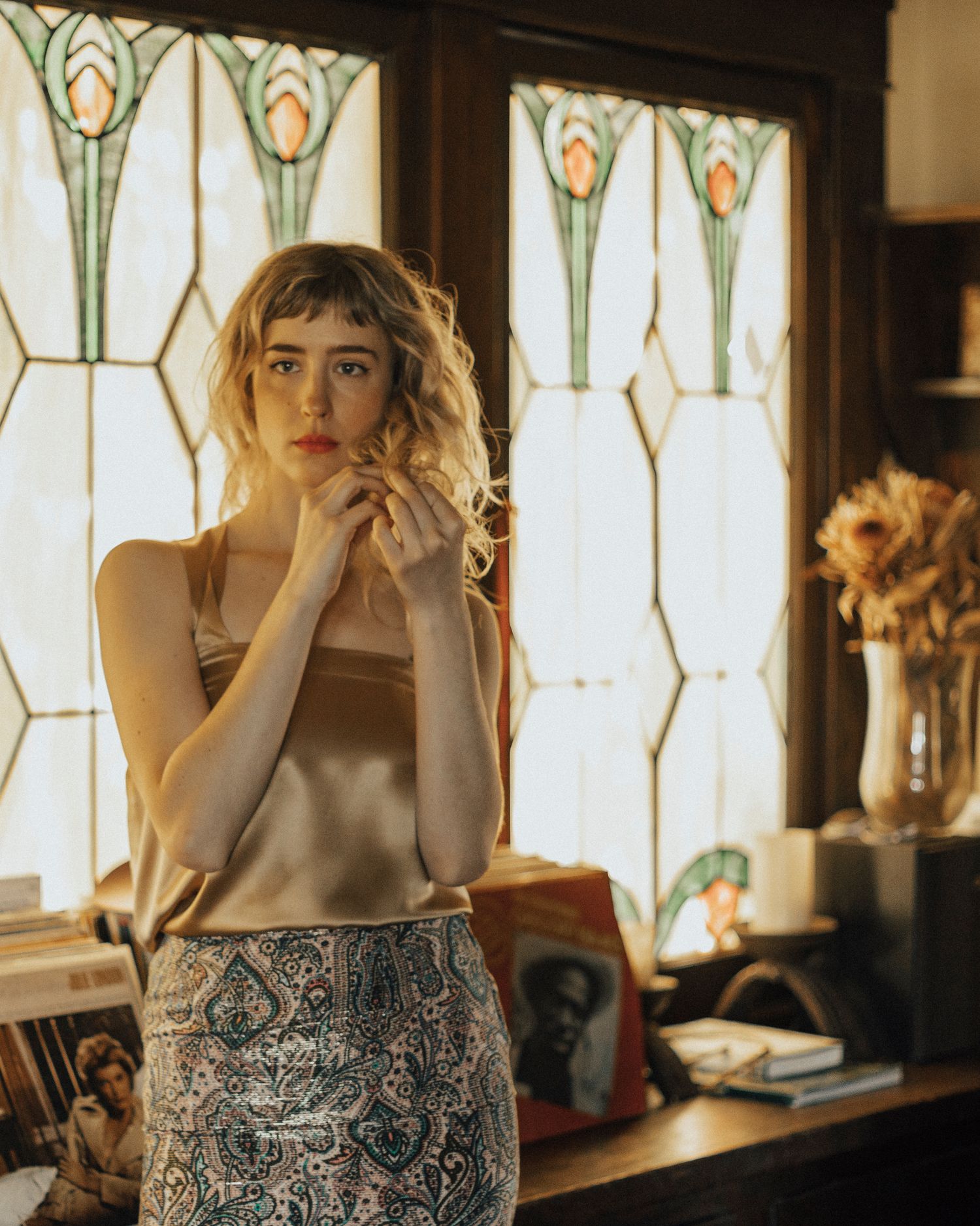 A sequence of moody indoor portraits featuring someone wearing a patterned dress against a window with decorative glass panels.