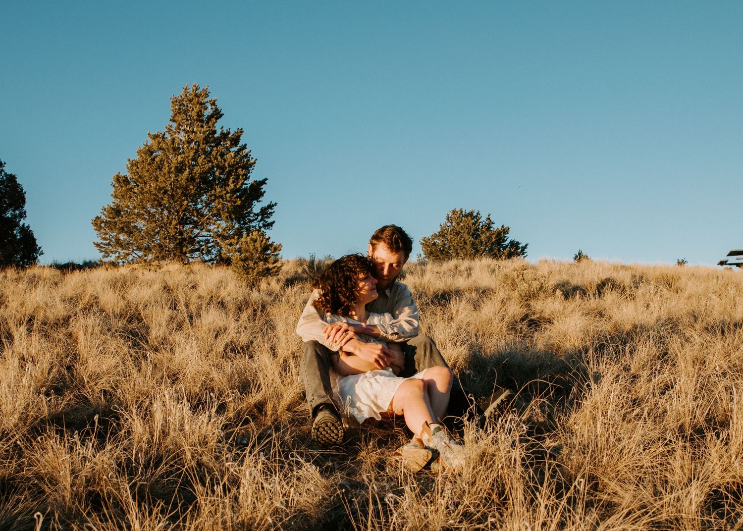 Engagement session in Taos New Mexico with couple embracing on a hillside in warm golden light