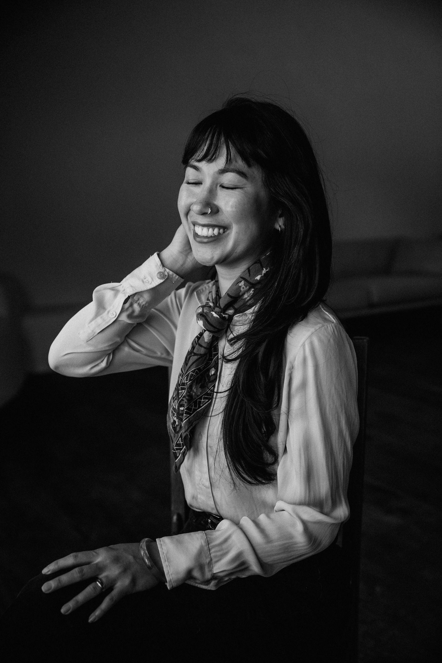 Black and white portrait of a smiling Asian woman with long hair, wearing a blouse and neck scarf.