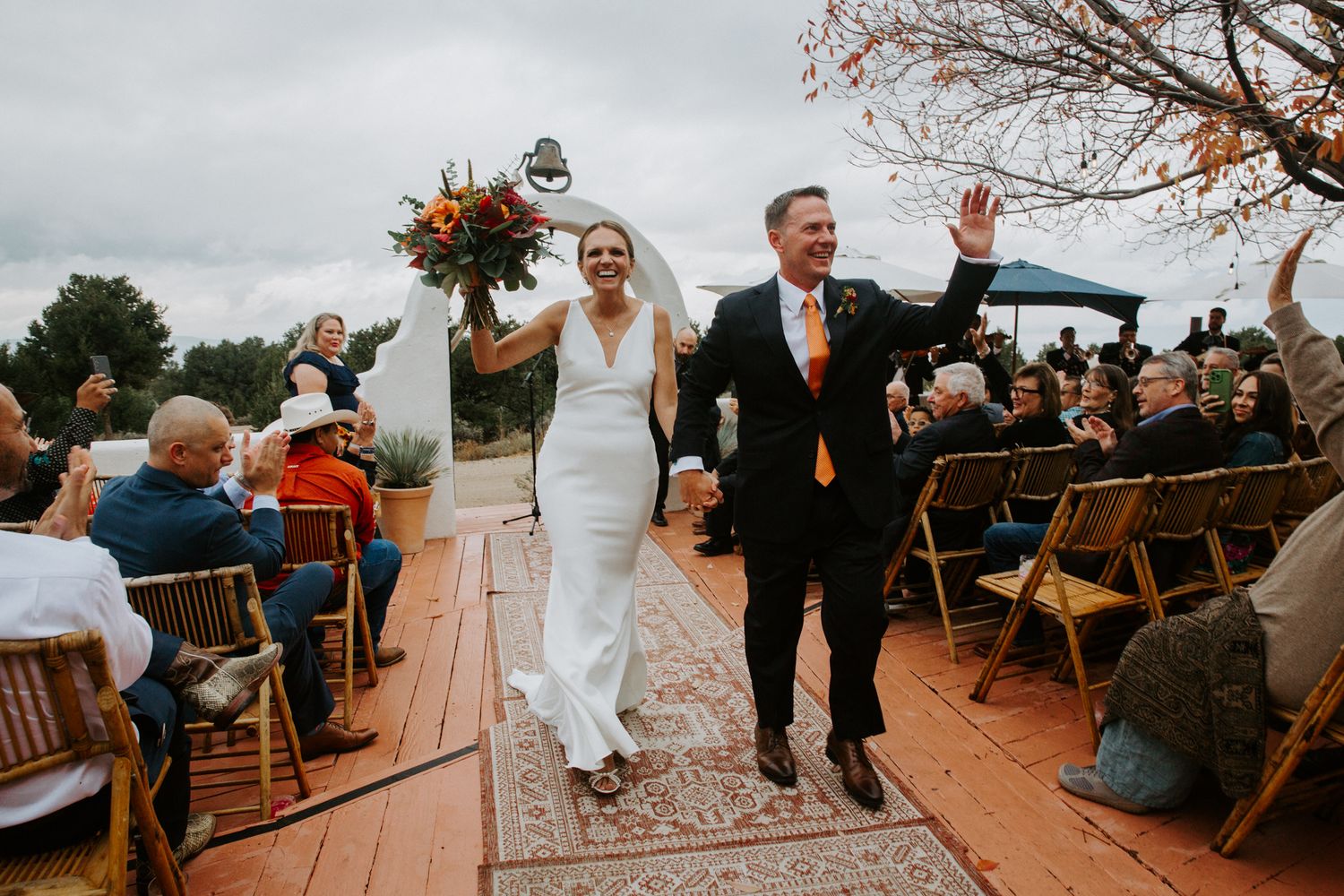 Wedding celebration at an outdoor venue during autumn with wooden chairs and fall foliage in the background.