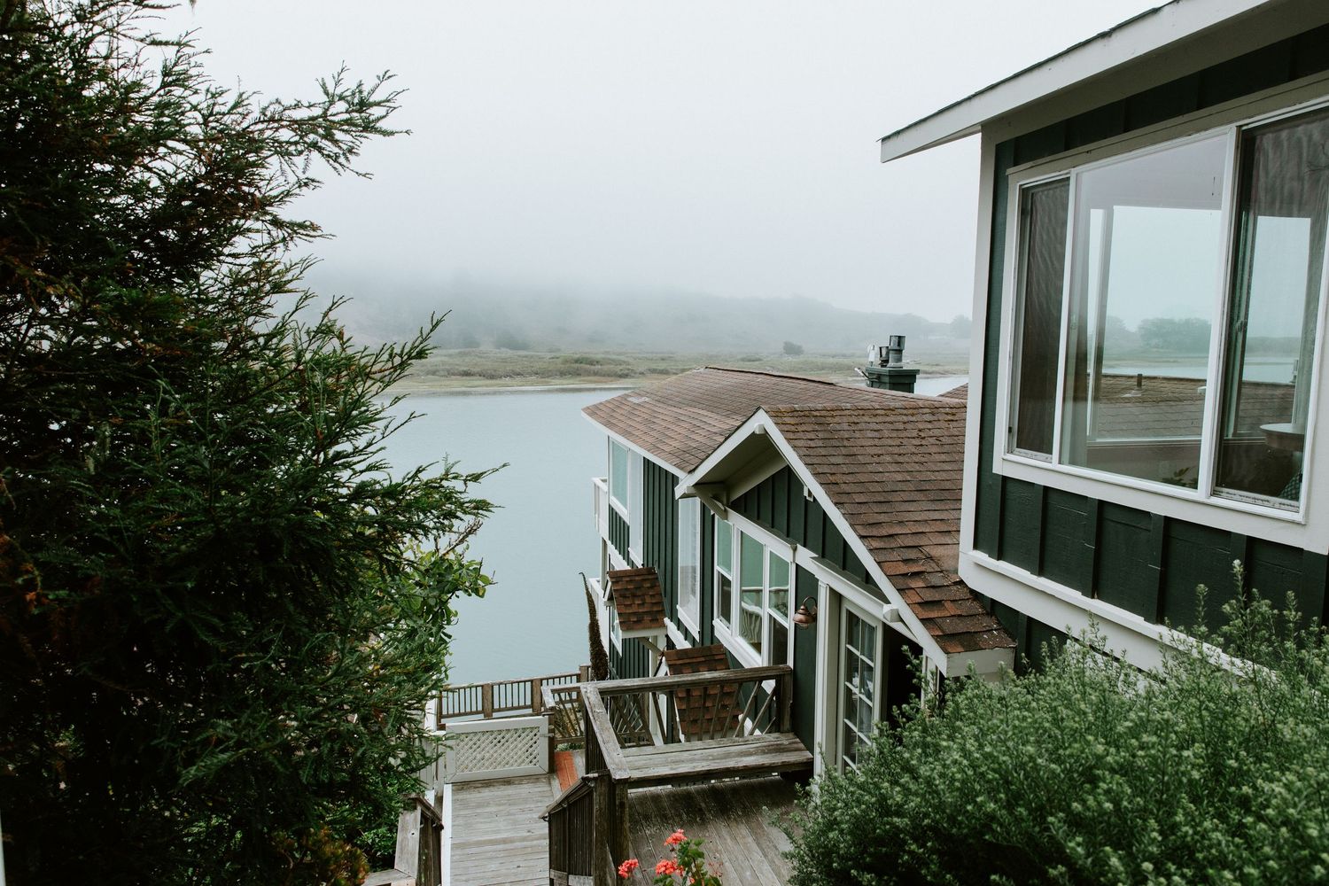 Coastal cottage with large windows overlooking a misty bay and rocky shoreline.