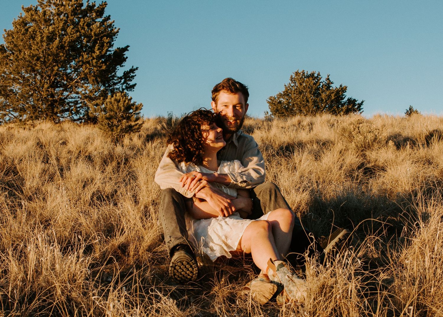 Couple embracing during golden hour engagement session in Taos NM surrounded by tall desert grass and evergreens