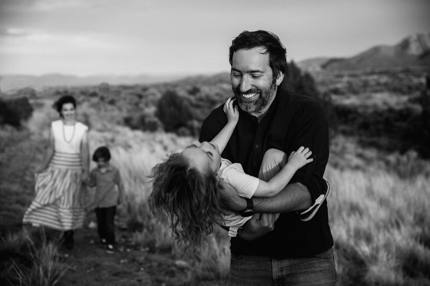 Candid black and white photos of family playtime outdoors in desert landscape.