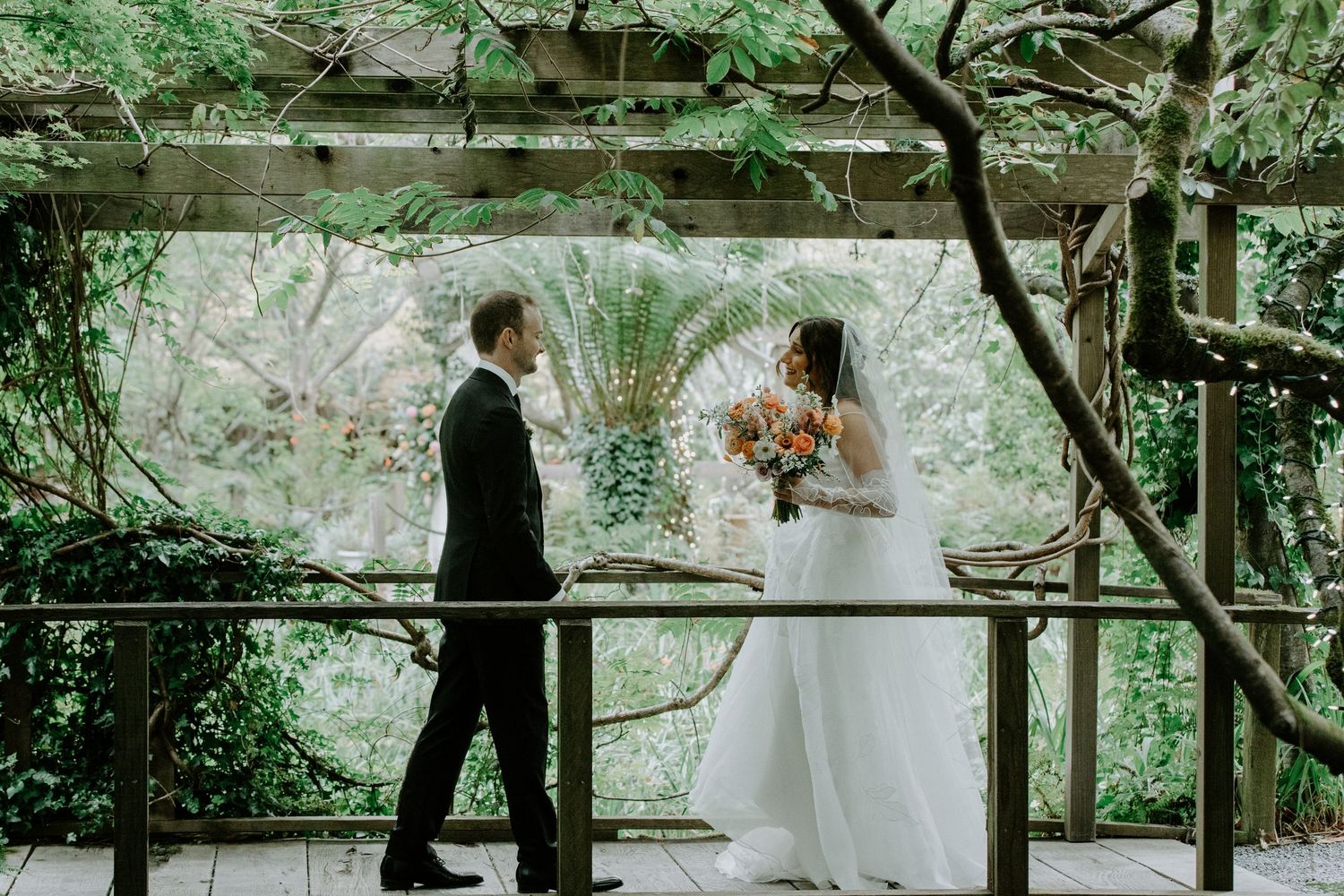 A couple shares a romantic moment on a wooden bridge surrounded by lush greenery during their outdoor wedding ceremony.