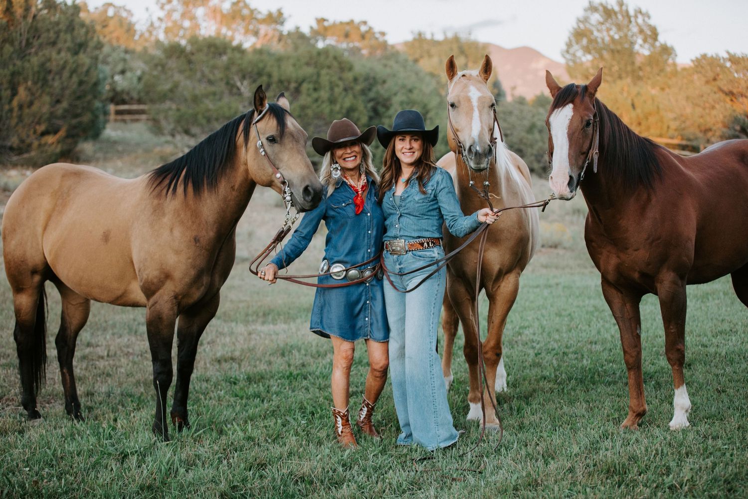 Western lifestyle session in Taos New Mexico with two women in denim standing with horses in a sunlit field