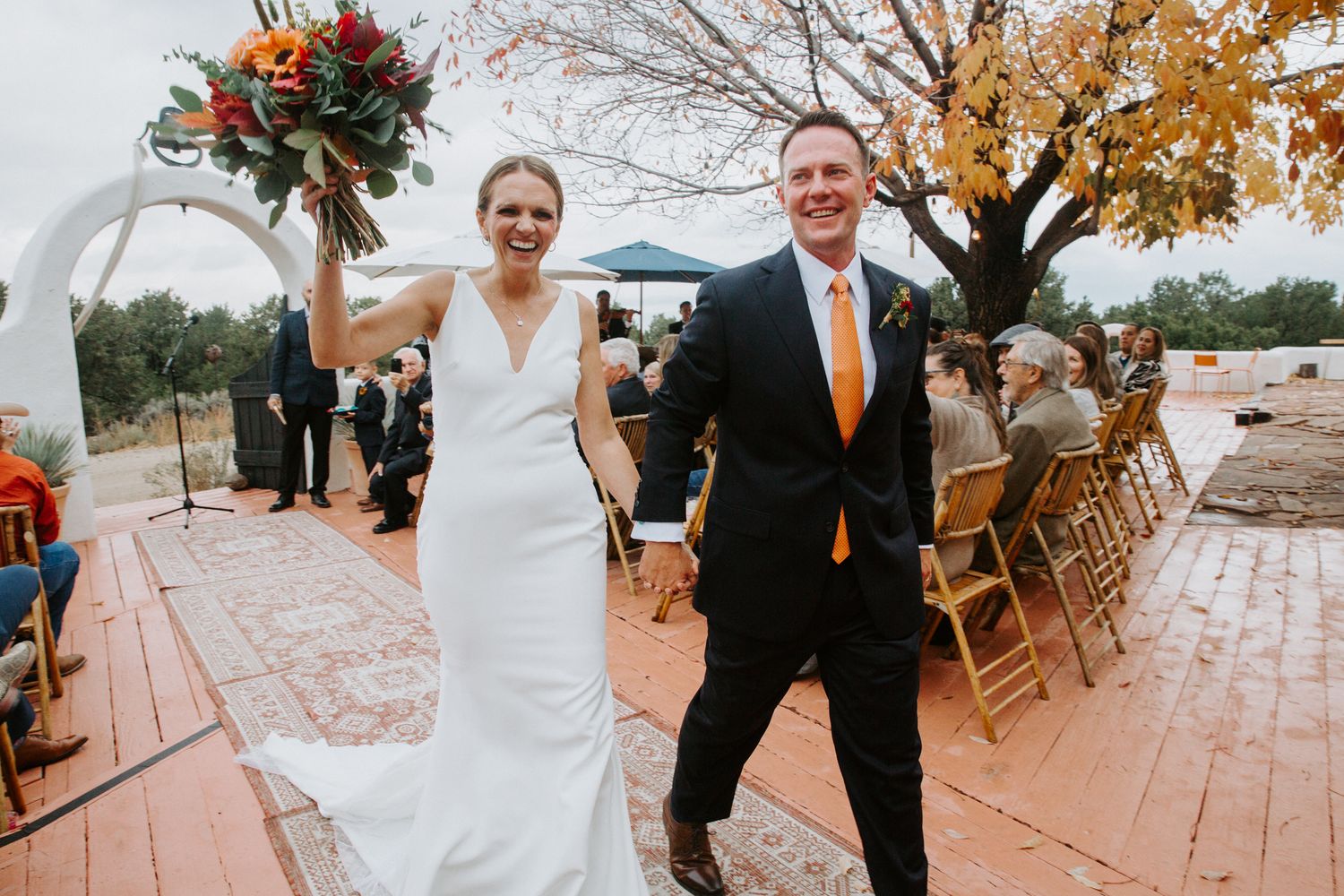 Wedding celebration on a wooden deck surrounded by autumn trees with orange and brown foliage.