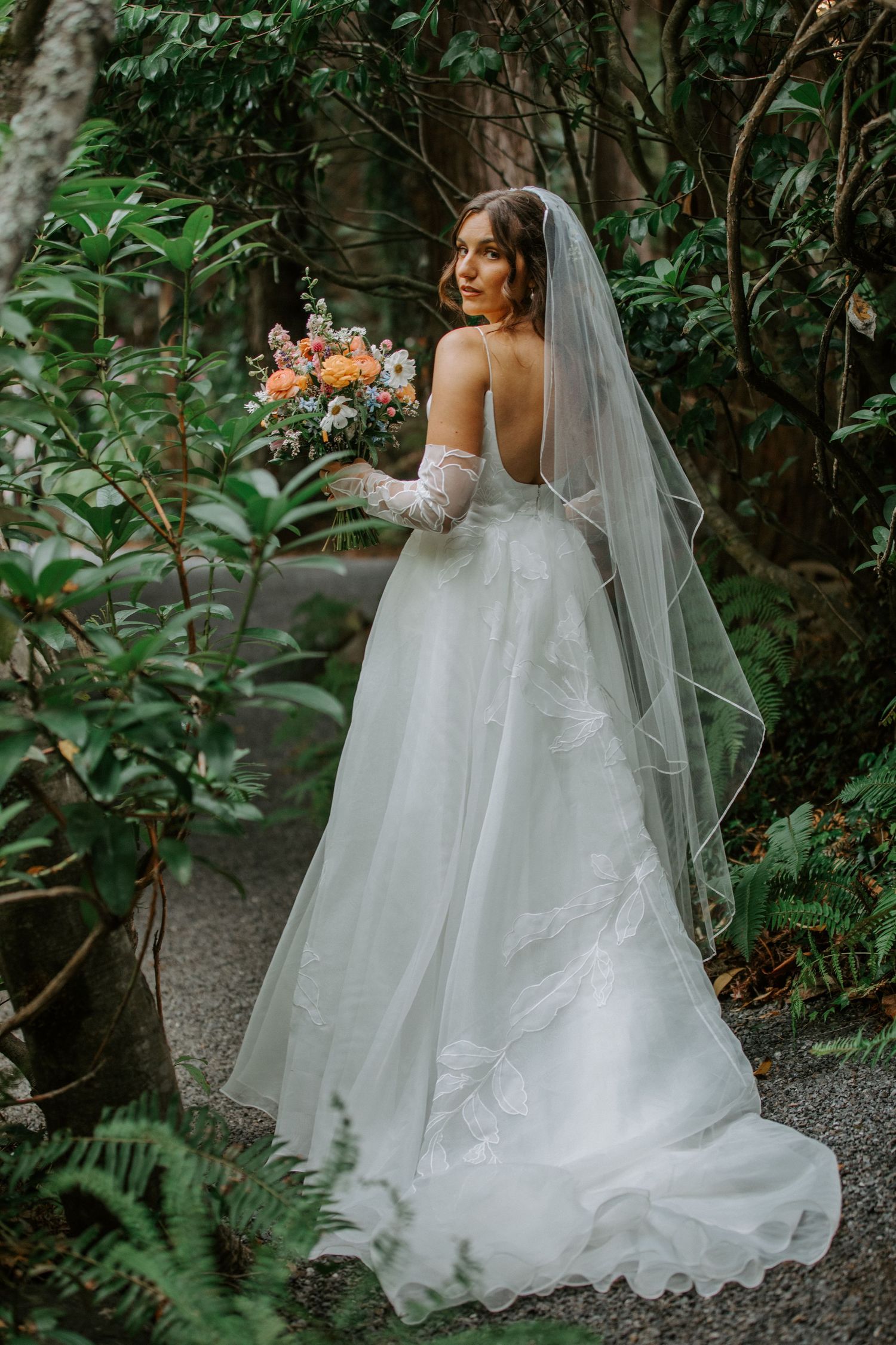 Flowing white wedding dress with long veil captured in a lush garden setting.