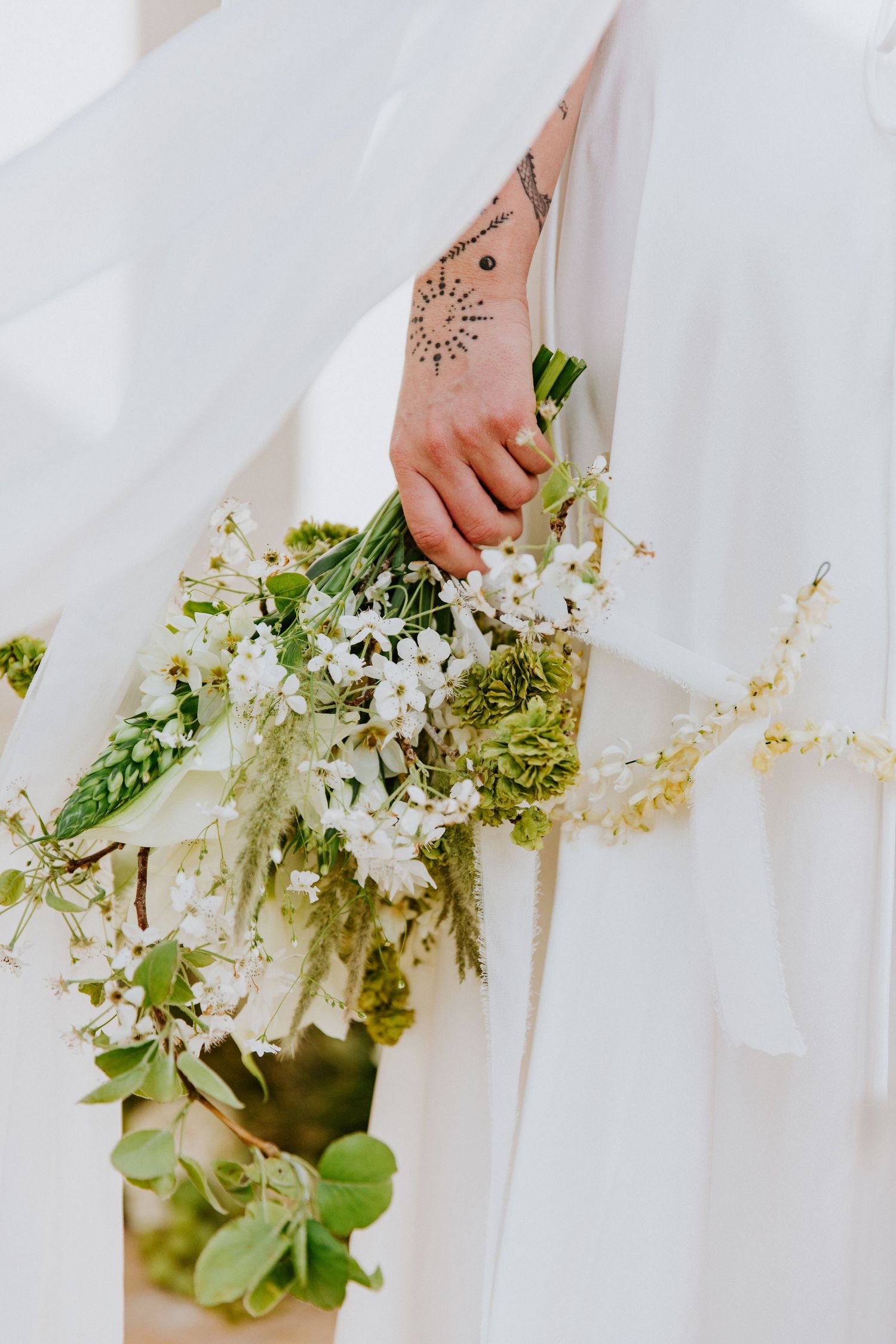 Delicate white floral bouquet with cascading greenery held against a flowing white dress.