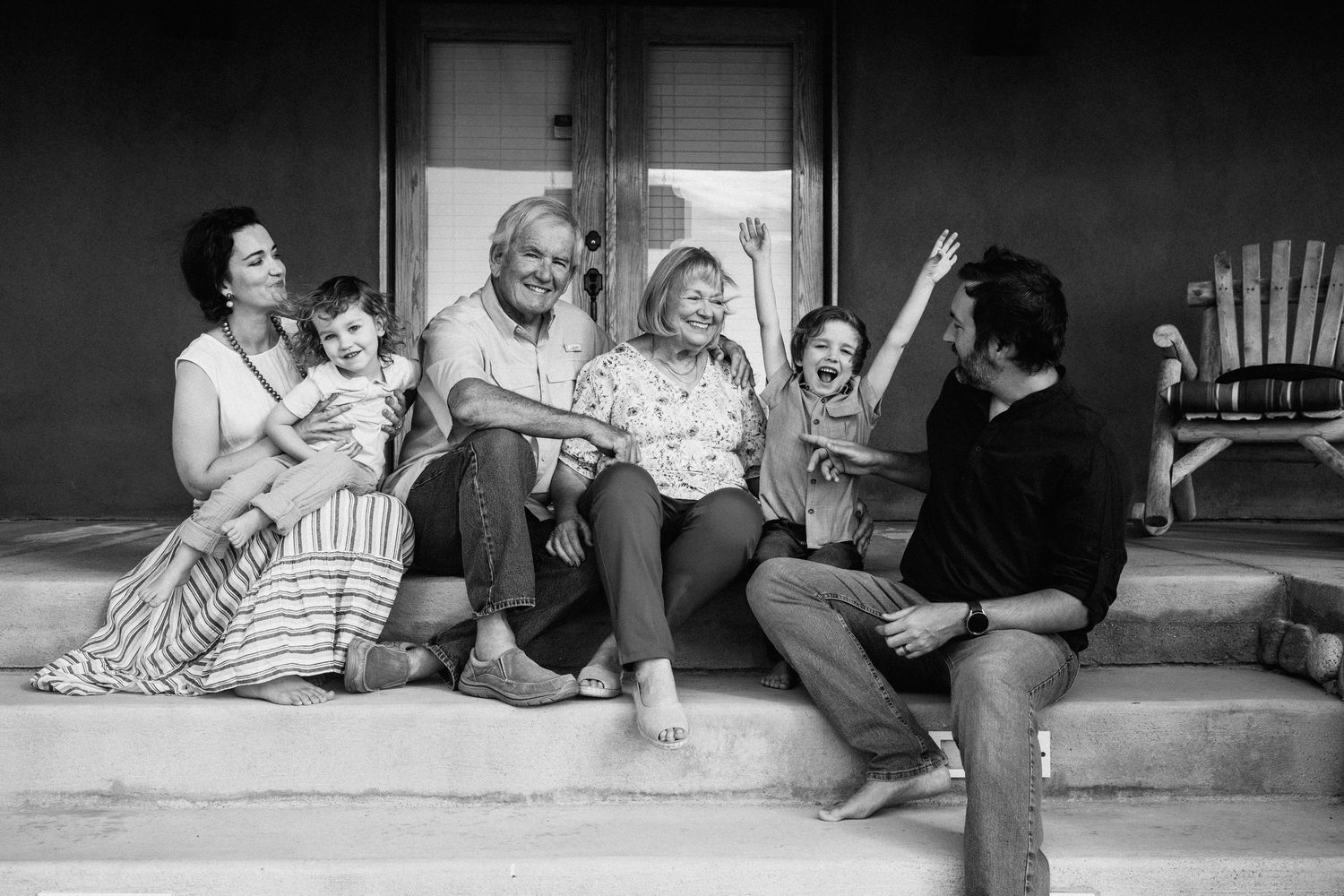 Black and white photo of multi-generational family gathering on front porch steps.