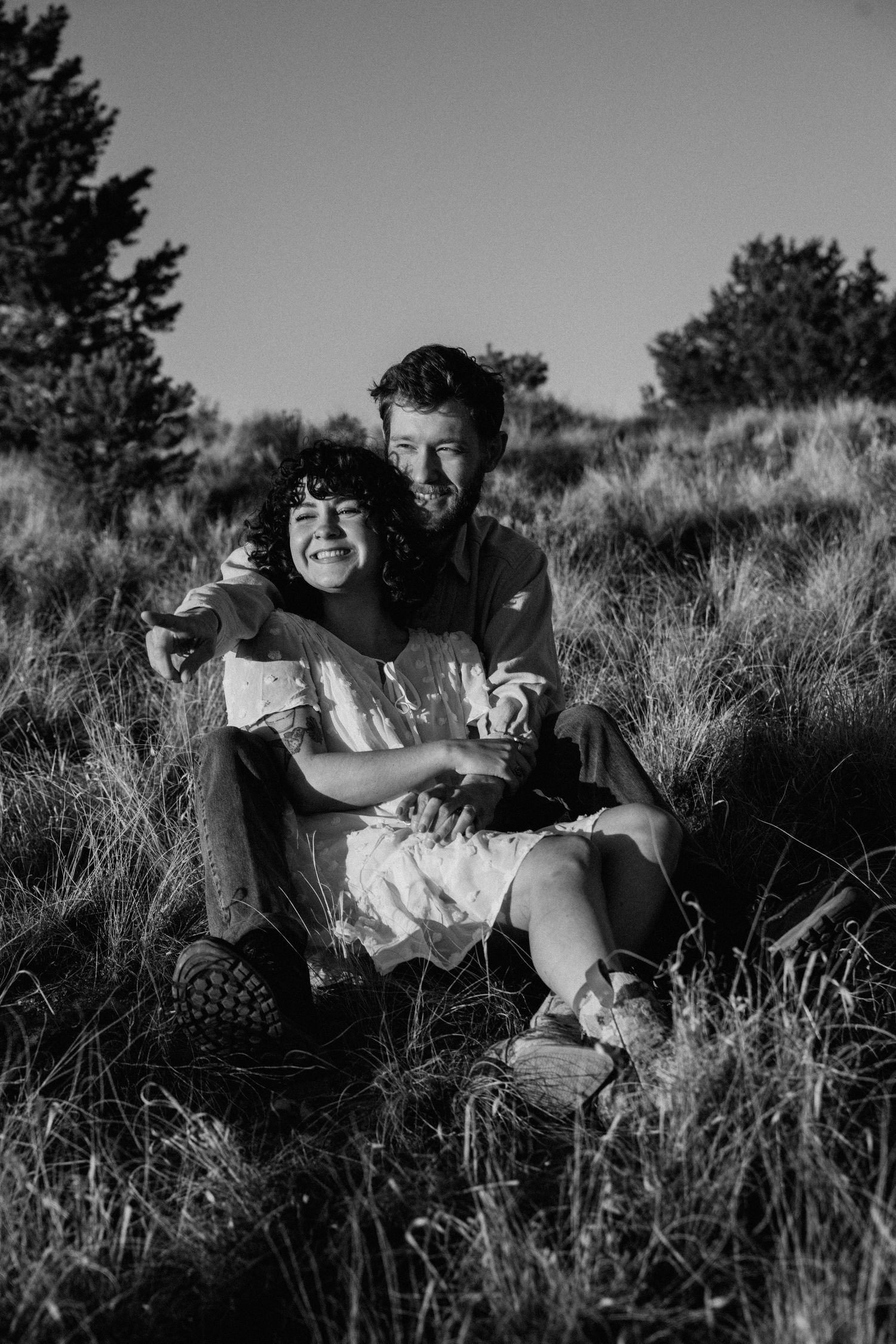Black and white engagement session in Taos, New Mexico with couple sitting together in a grassy field