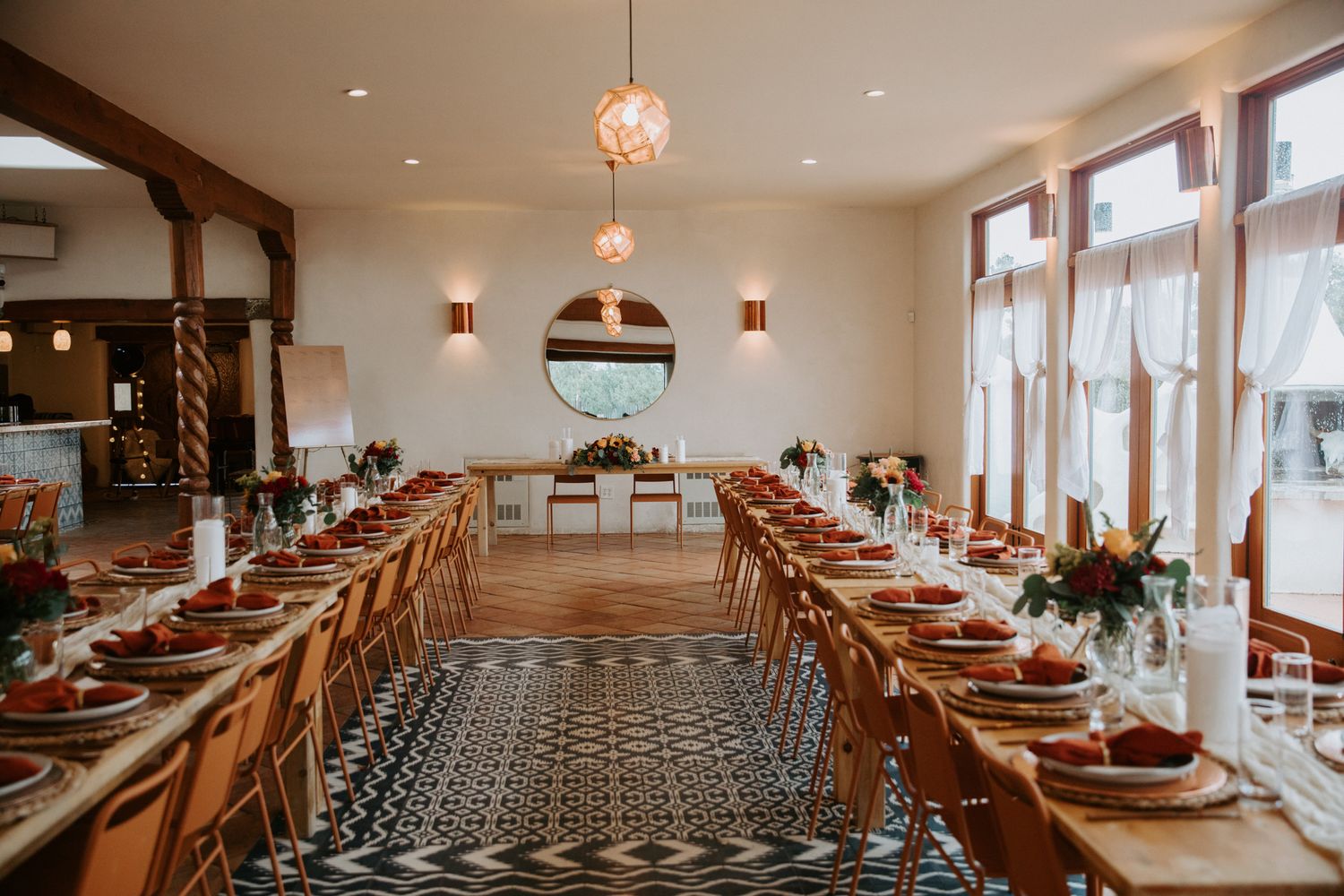 A rustic wedding reception venue with long wooden tables, patterned floor tiles, and elegant table settings.