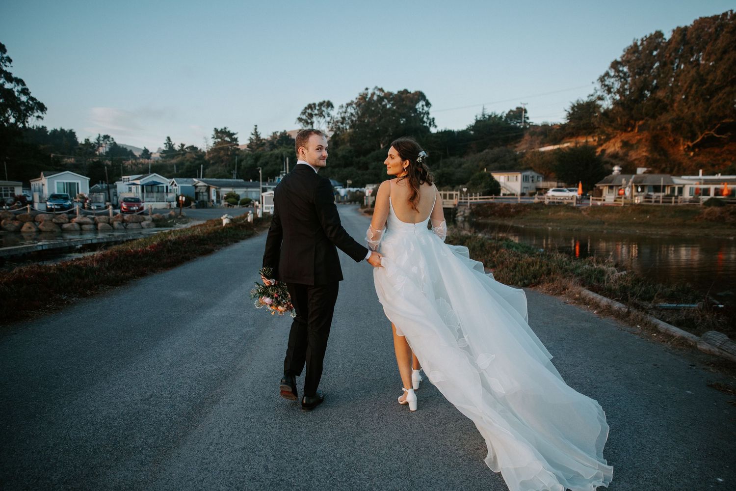 Newlyweds strolling along marina walkway during golden hour.