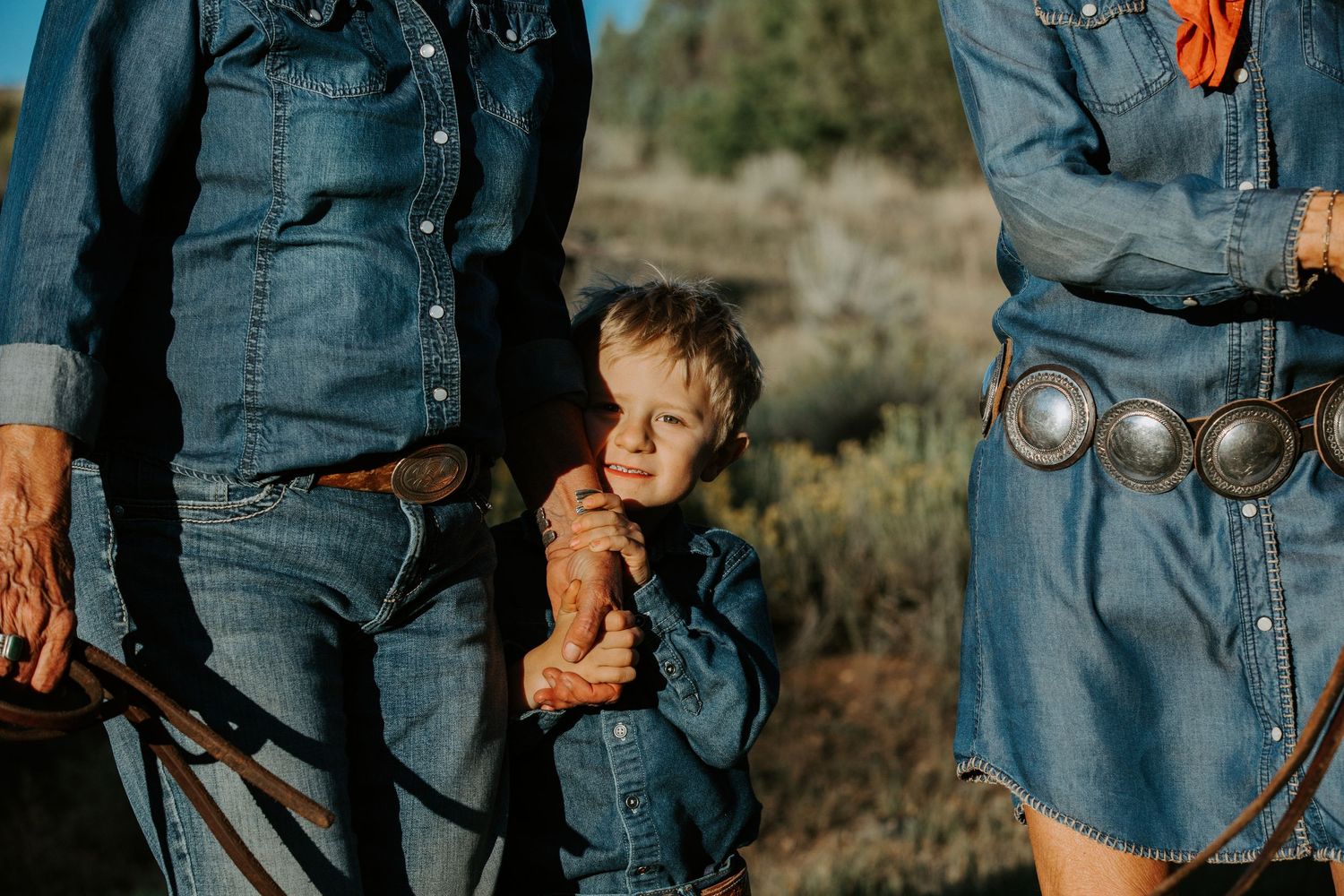 A young child stands between adults wearing denim in an outdoor setting.