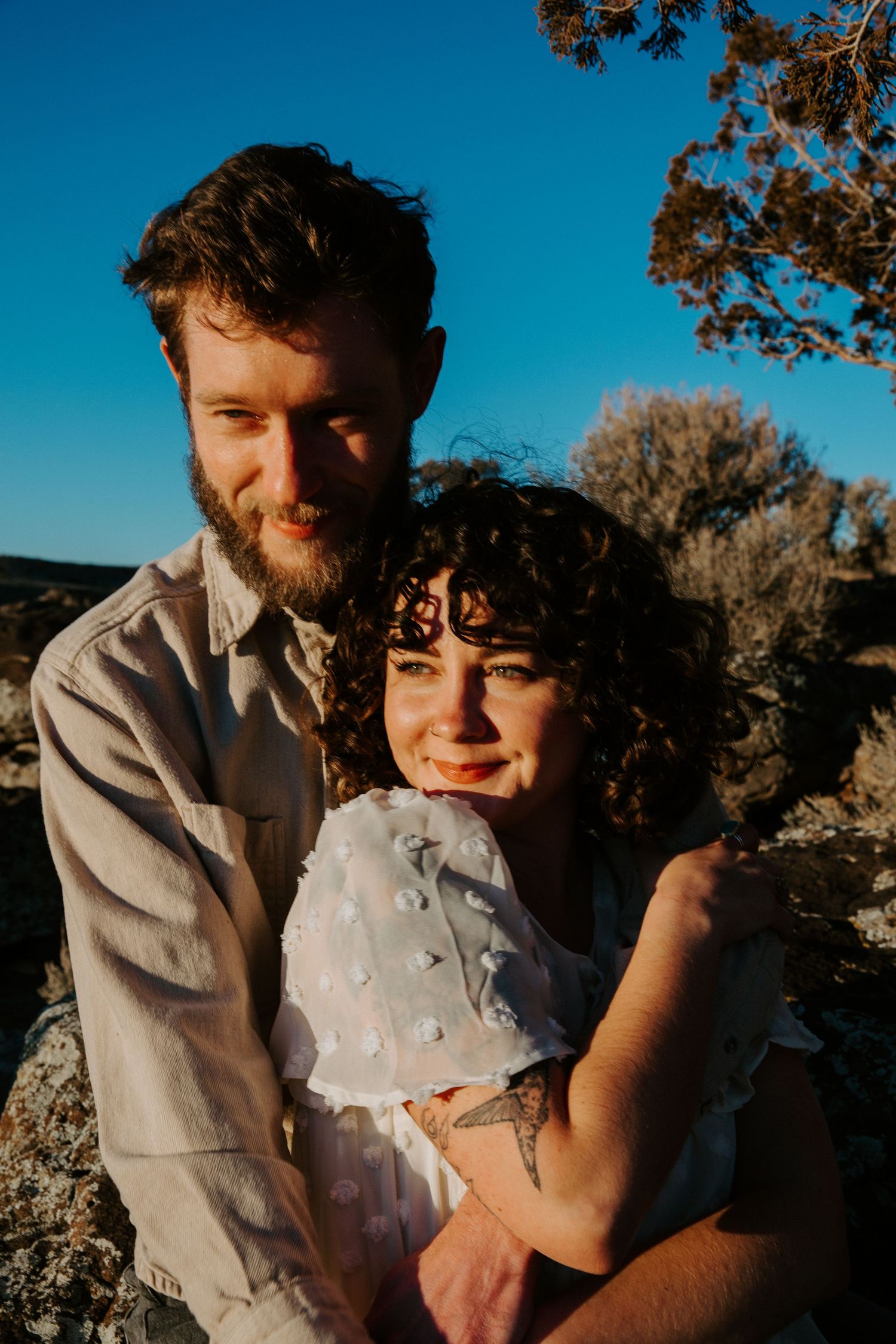 Couple embracing during golden hour engagement session in Taos New Mexico with blue sky and desert landscape